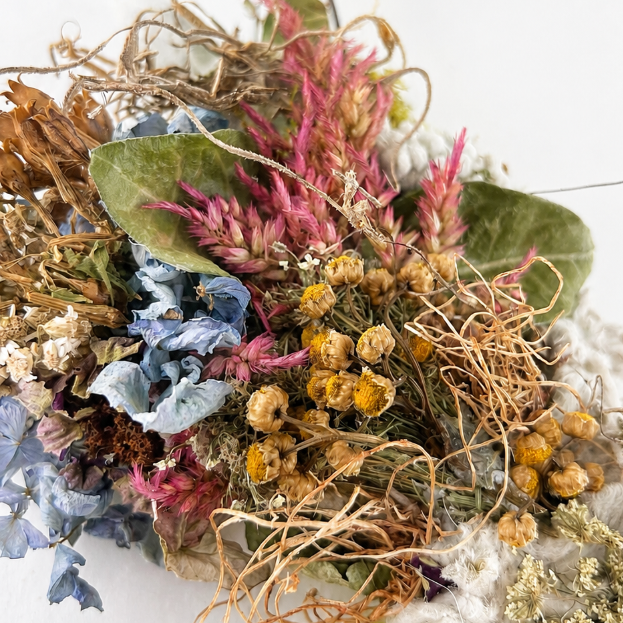 Close-up of dried blue flowers, pink botanicals, golden blooms and greenery in a handmade wall hanging