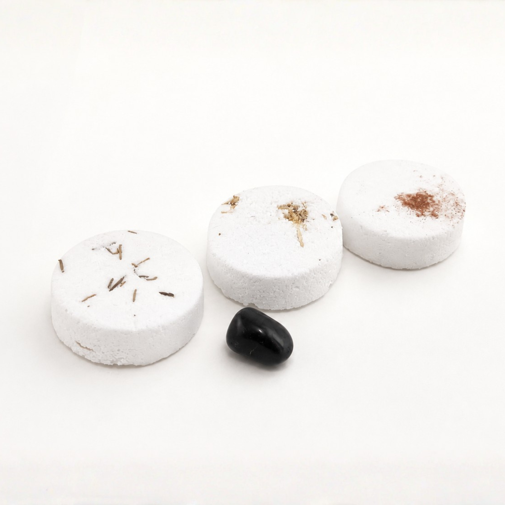 Three handcrafted Christmas shower steamers with rosemary, marshmallow and cinnamon botanicals displayed beside a polished black stone on a clean white background.