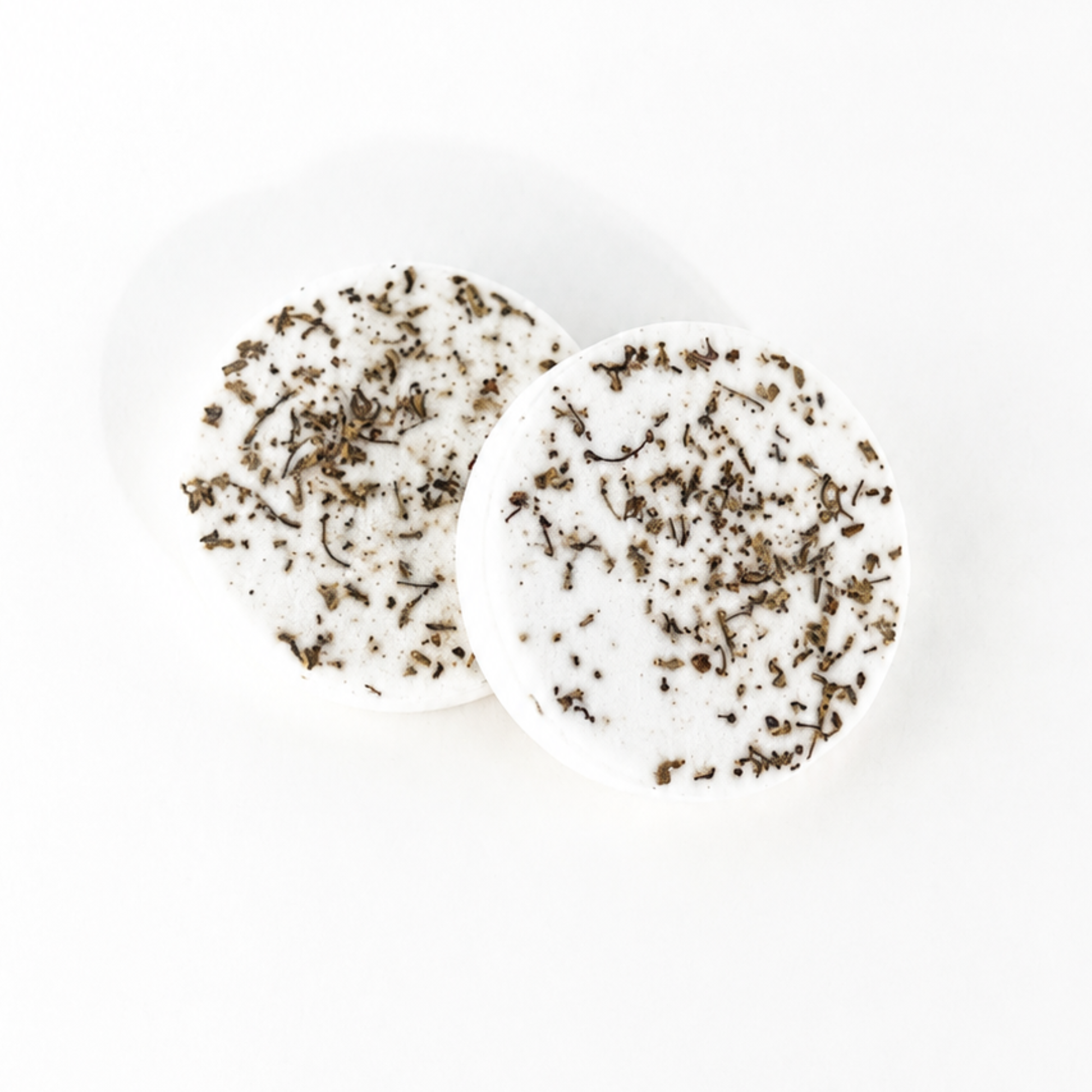 Two handcrafted botanical shower steamers decorated with dried flowers and botanicals on a white background.