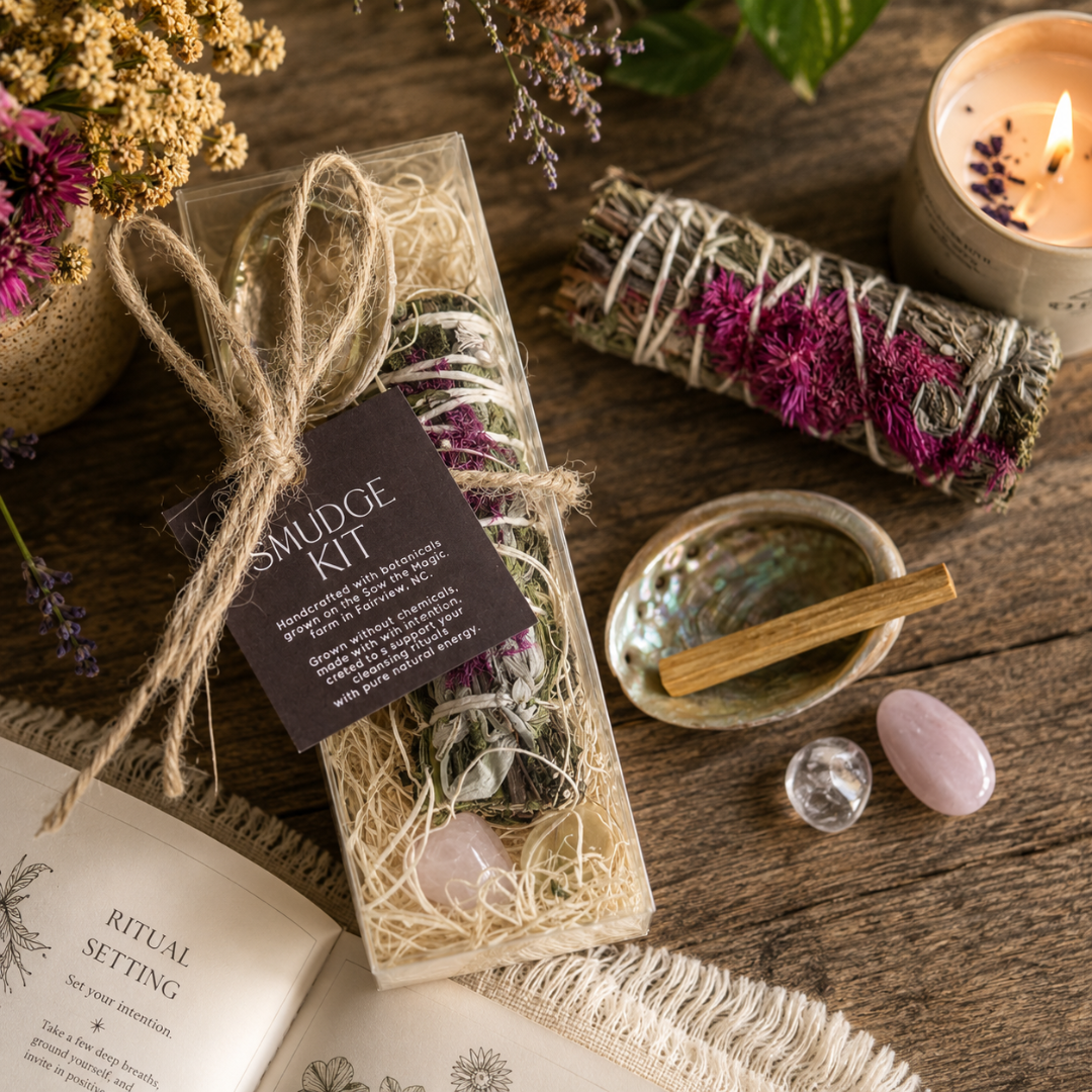 Handcrafted botanical smudge ritual kit displayed on a rustic wooden table with a white sage bundle wrapped in pink botanicals, abalone shell, palo santo stick, rose quartz, clear quartz crystal, dried flowers and a softly glowing candle. The cozy lifestyle scene highlights a natural cleansing and meditation ritual inspired by mindful living and botanical wellness.