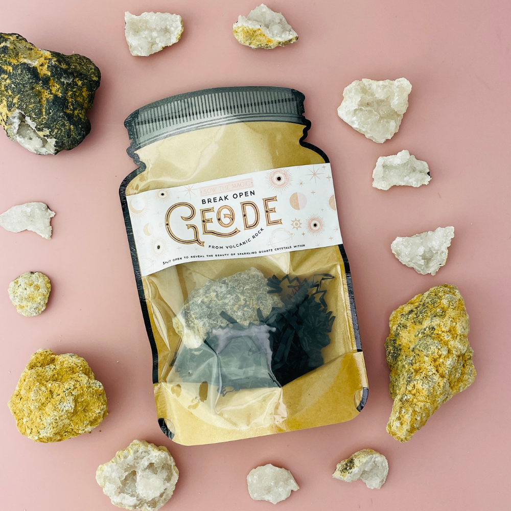 Break-open geode rock surrounded by natural crystals and stones on pink backdrop