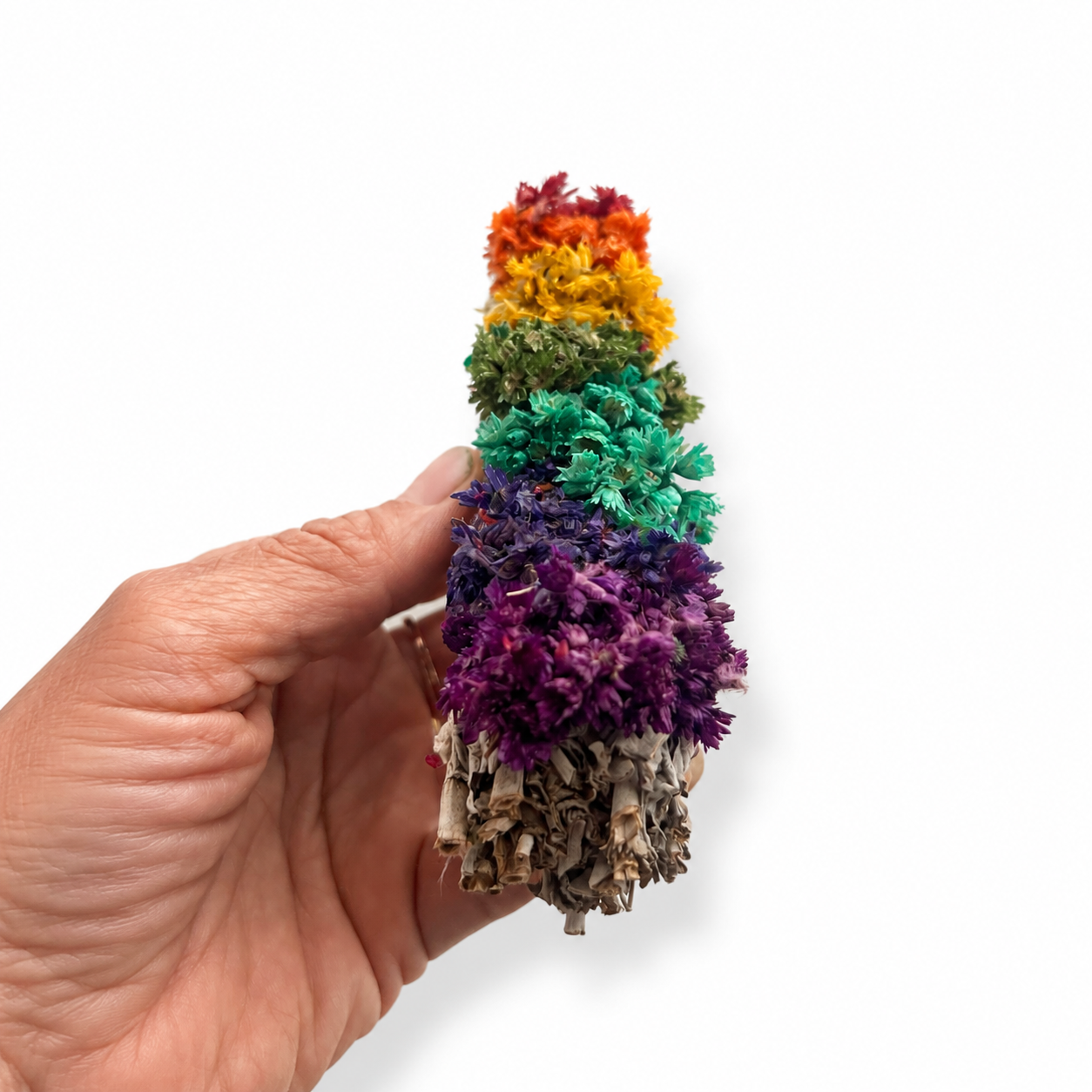 Hand holding a white sage smudge stick decorated with colorful chakra-inspired dried flowers