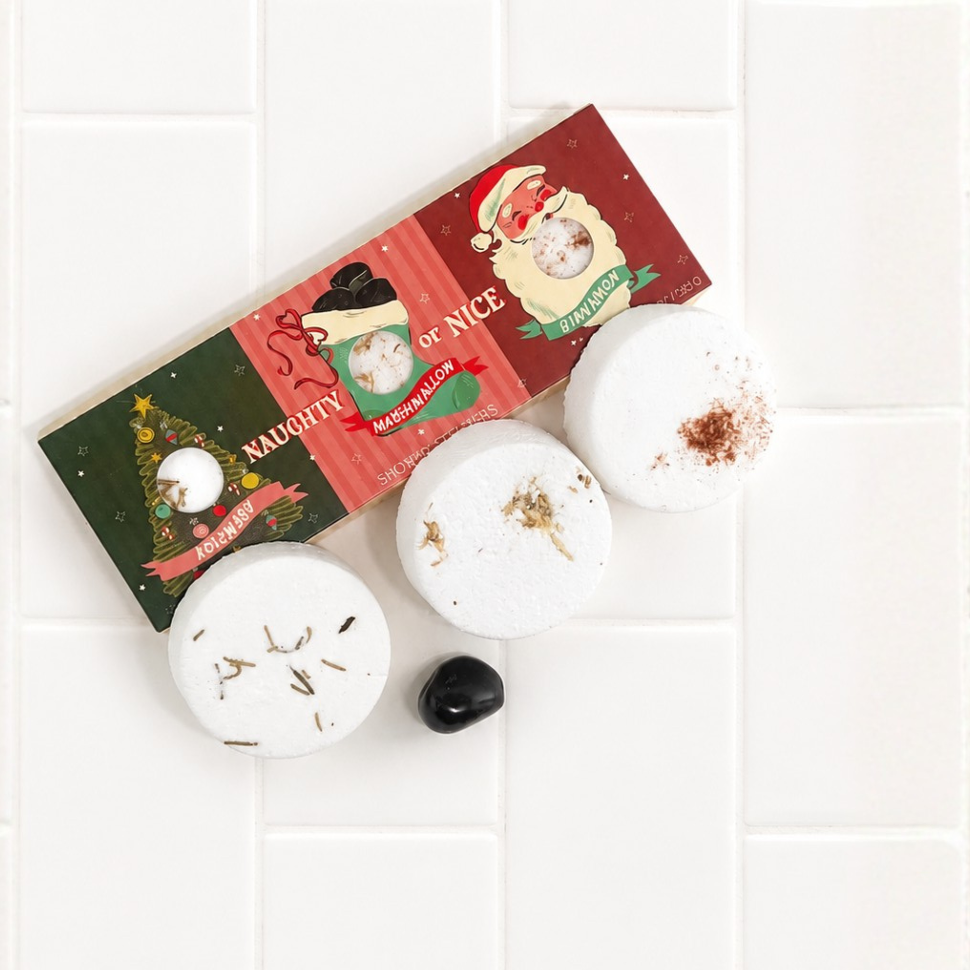Flat lay of the Sow the Magic Naughty or Nice Christmas Shower Steamer gift set with three botanical shower steamers arranged on bright white tile.