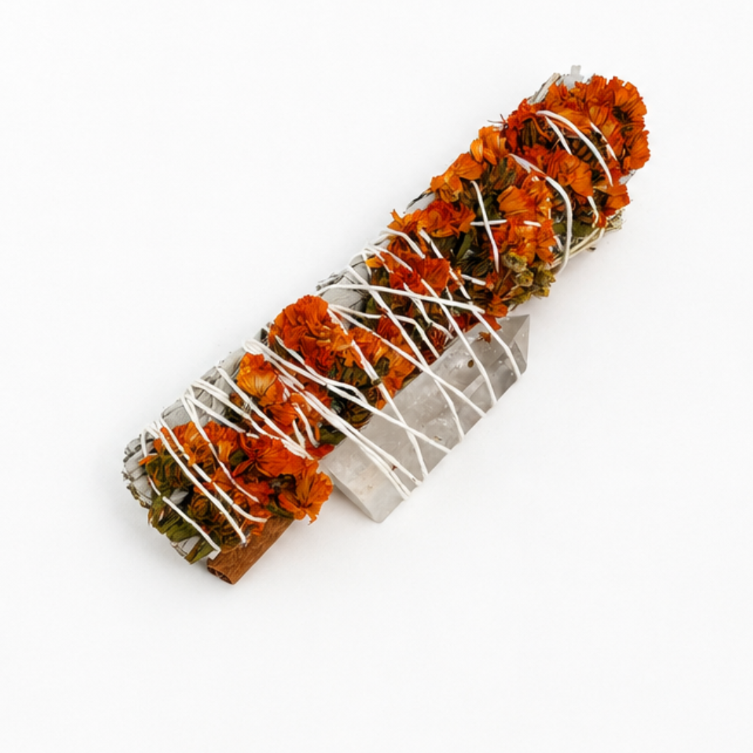 Handcrafted 6-inch White Sage smudge stick wrapped with orange sinuata flowers, a cinnamon stick and a Clear Quartz crystal point. Handmade botanical ritual bundle on a white background by Sow the Magic®.