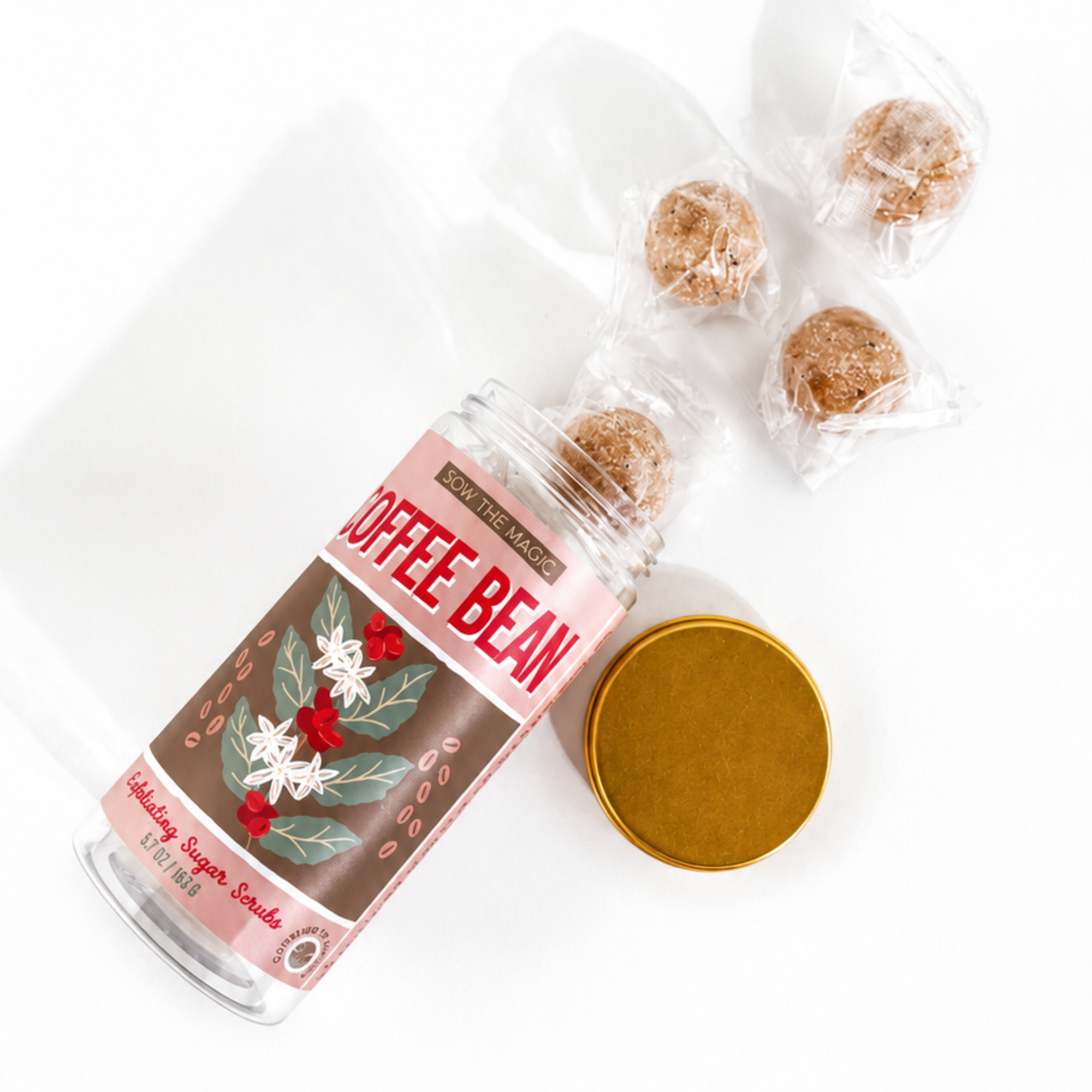 Coffee Bean Exfoliating Sugar Scrubs spilling from a reusable jar with gold lid and individually wrapped scrub cubes.
