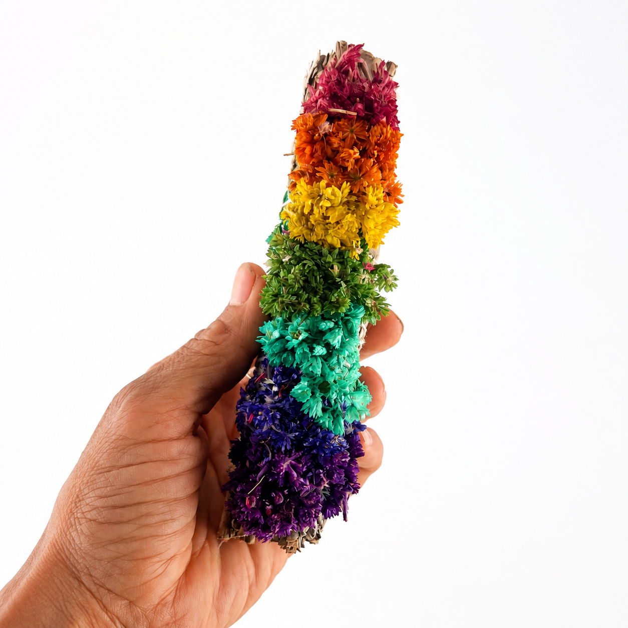 Hand holding a 6 inch white sage bundle decorated with rainbow chakra colored sinuata flowers