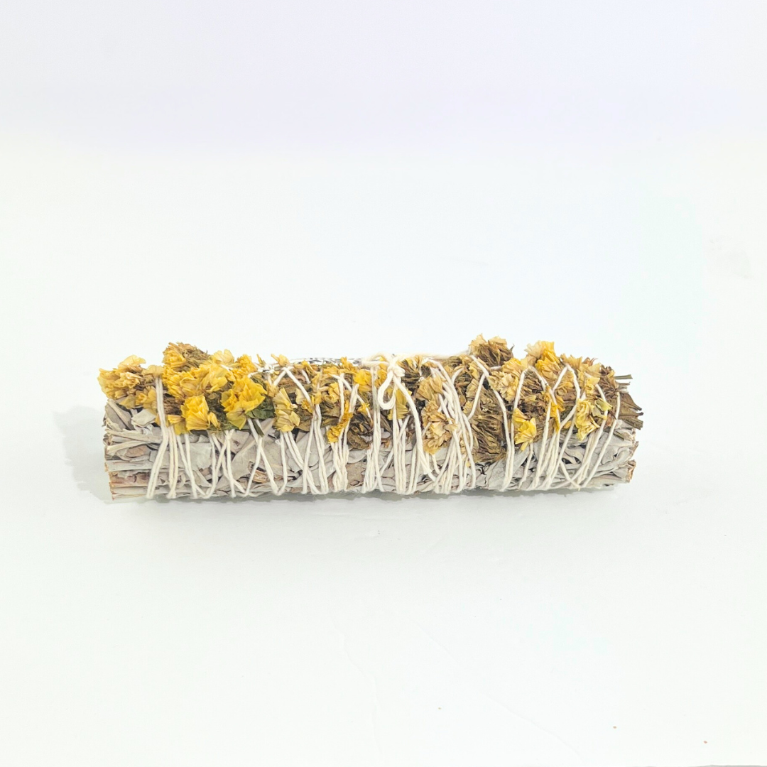 Handcrafted White Sage smudge stick wrapped with Palo Santo, yellow sinuata flowers and a silver feather charm. Handmade botanical ritual bundle on a bright white background by Sow the Magic®.