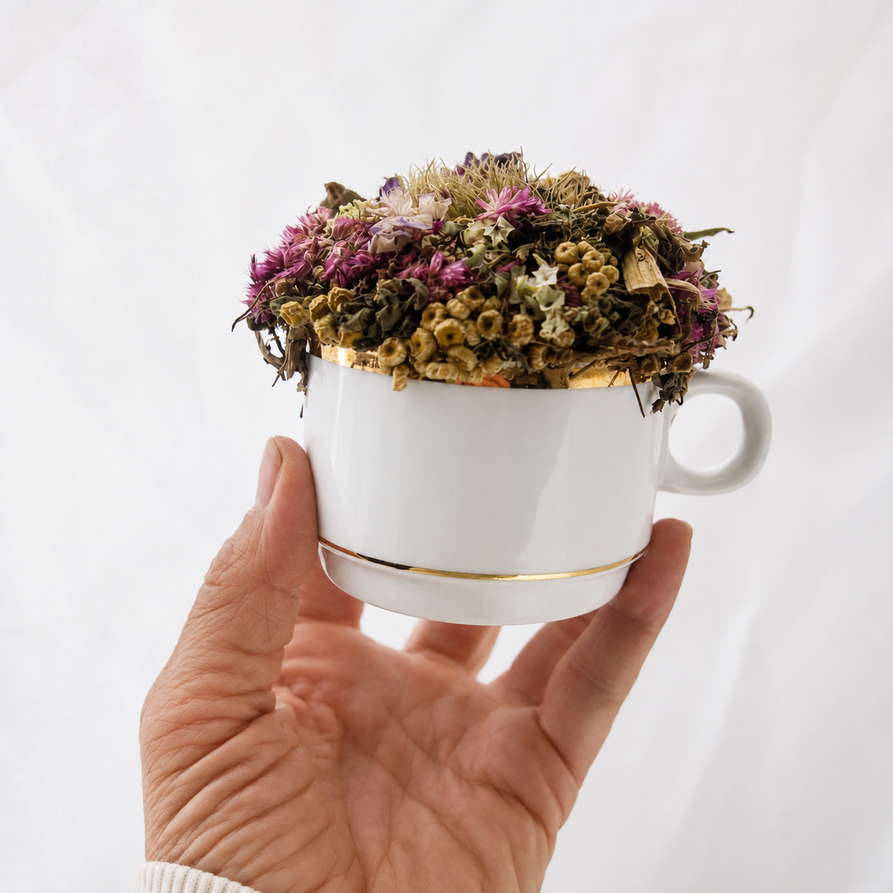 Petite February birth month dried flower arrangement held by hand in a vintage white teacup