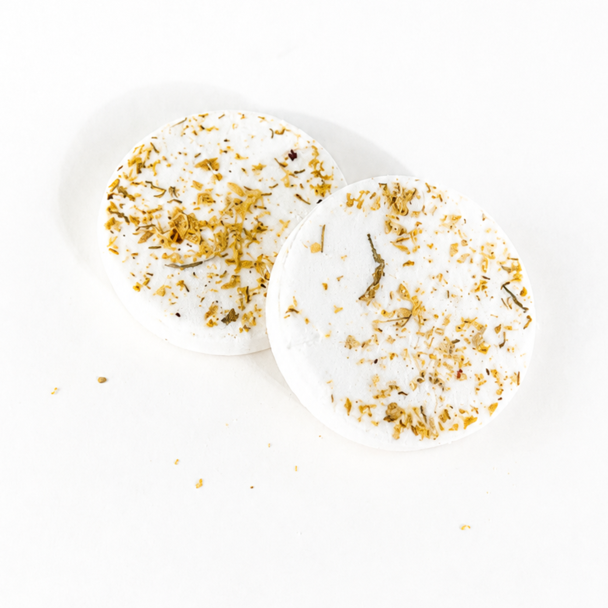 Two handcrafted Golden Honey shower steamers decorated with dried botanicals and flower petals on a white background.