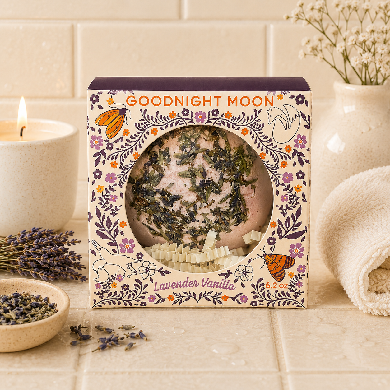 Goodnight Moon Lavender Vanilla botanical bath bomb gift box displayed on cream bathroom tile with a candle, fresh lavender, soft towel and calming spa décor in a relaxing bathroom setting.