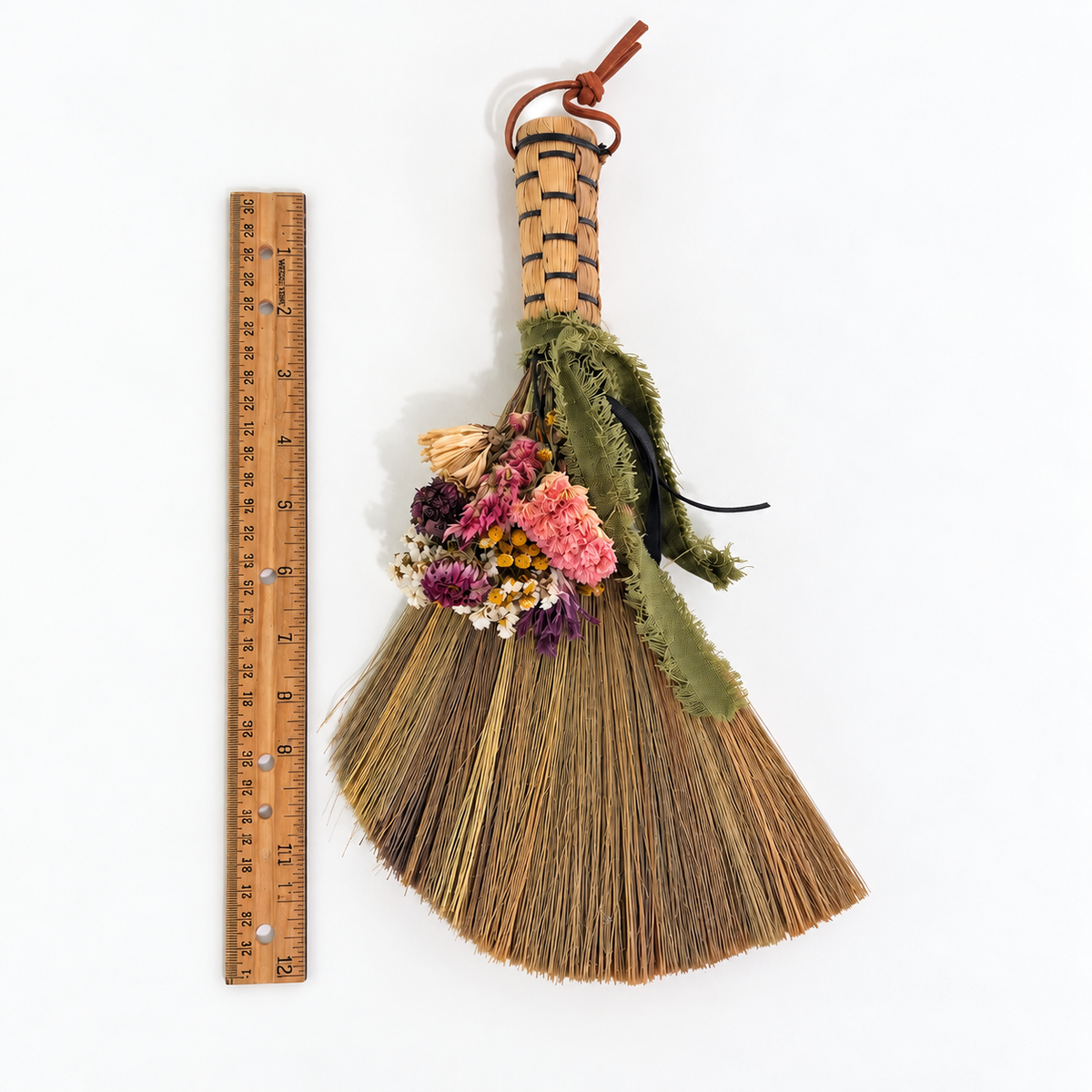 Handcrafted dried flower botanical broom displayed beside a 12-inch wooden ruler to show the size of this decorative straw whisk broom.