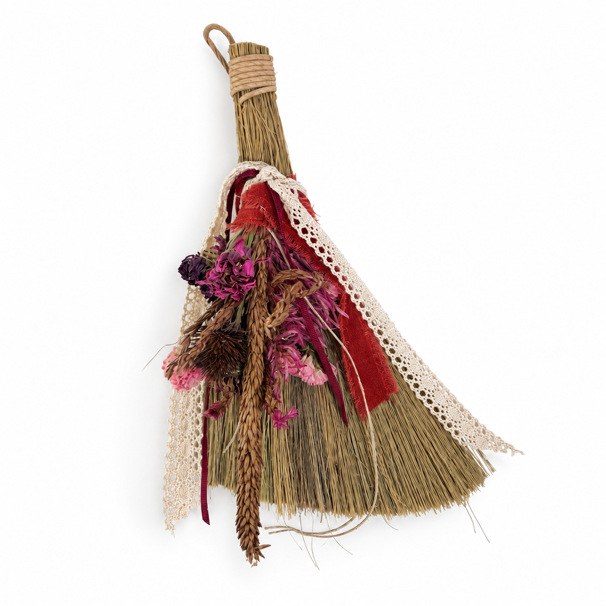Handmade straw botanical broom decorated with farm-grown dried flowers, red fabric and cream lace on a white background.