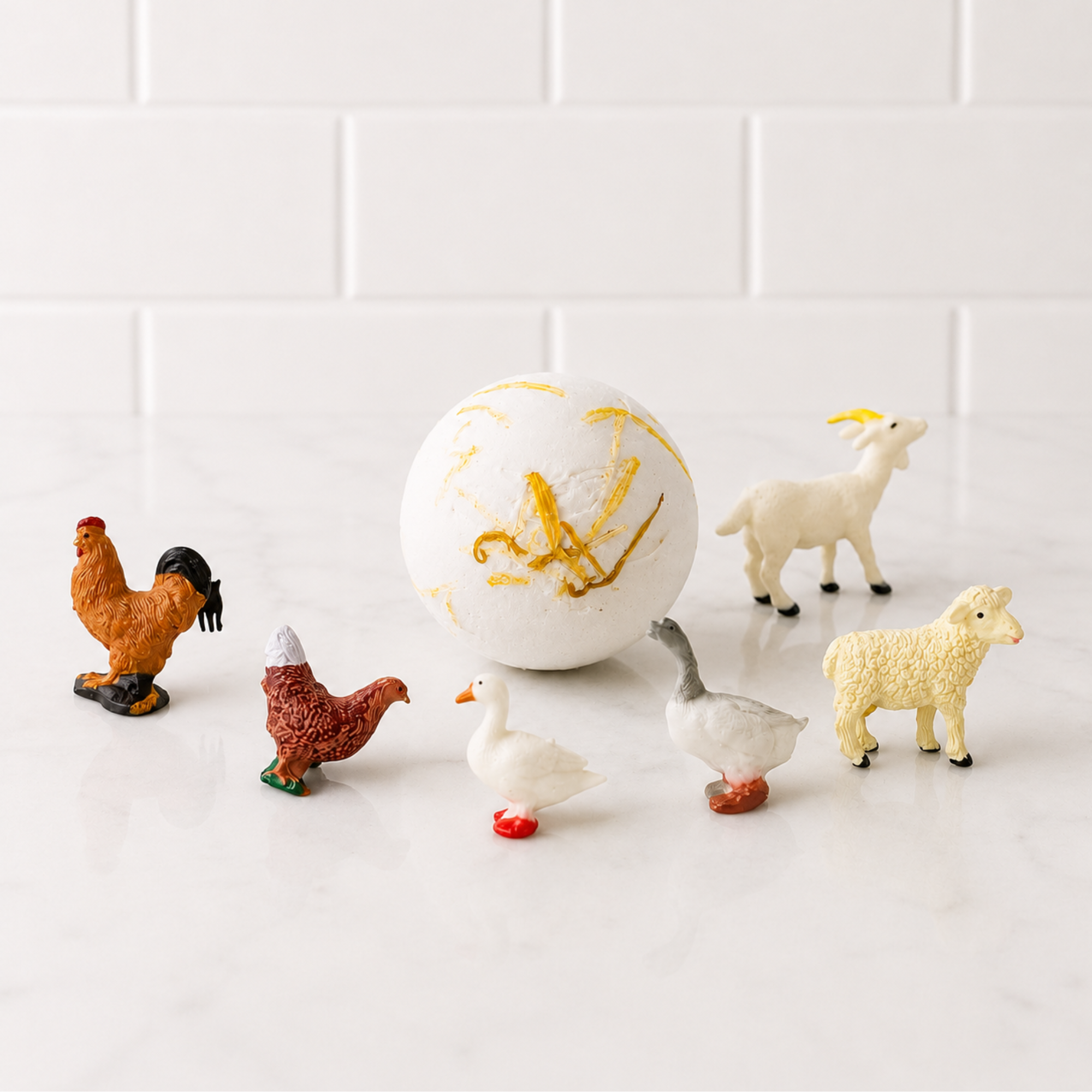 Sow the Magic® Honey Bath Bomb with hidden farm animal toy inside displayed beside its gift box on a white marble bathroom countertop. Kids surprise bath bomb made with natural ingredients and topped with real botanicals.