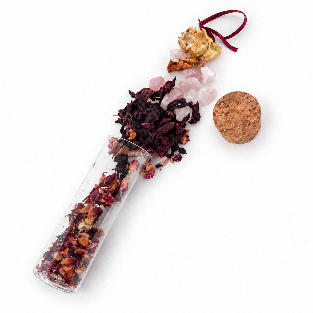 Dried flowers, herbs and tiny keepsakes spilling from an open A Token of Love intention vial beside its cork and pink tag.