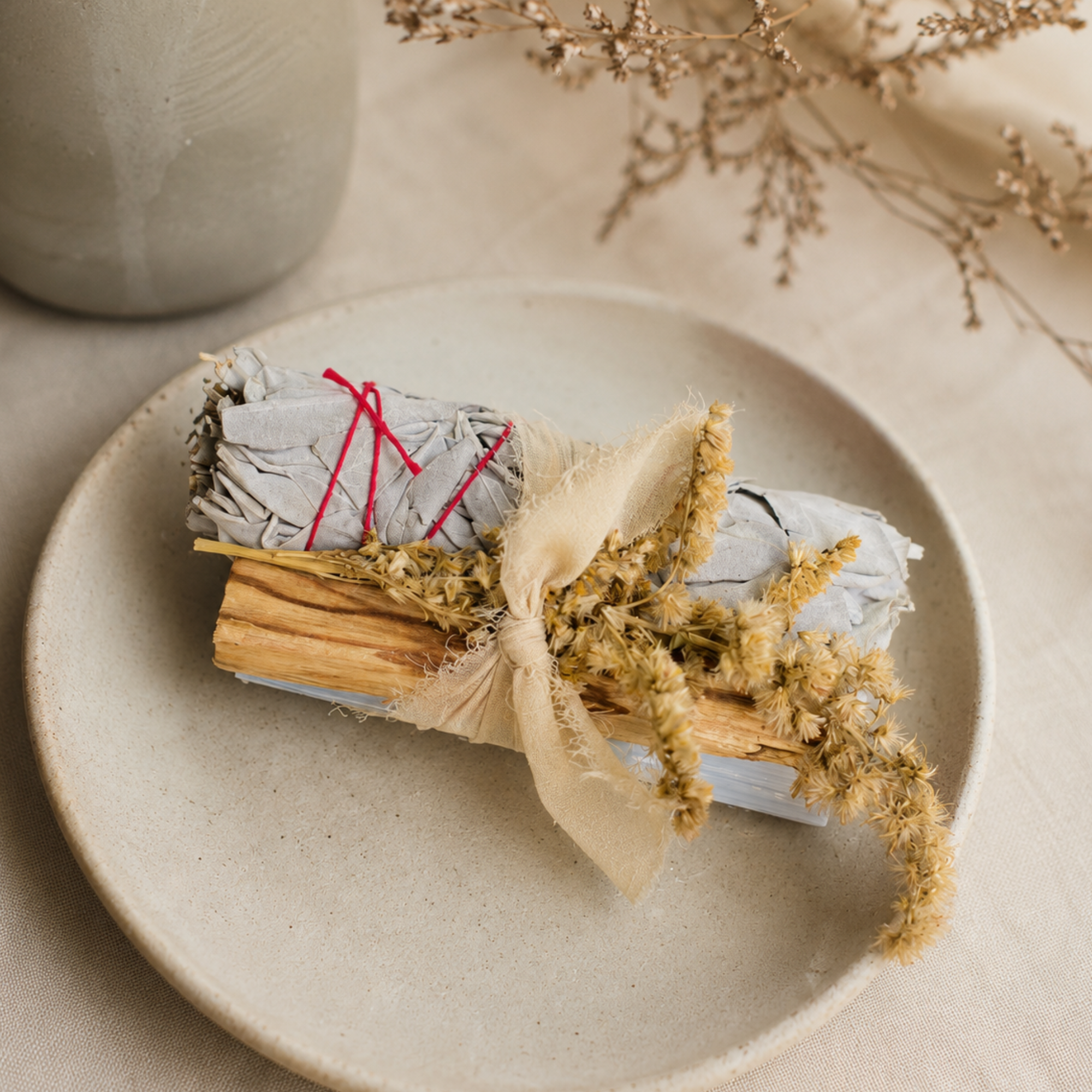 White sage protection bundle with palo santo, selenite crystal and dried goldenrod displayed on a ceramic dish with neutral linen for a calming home cleansing ritual.
