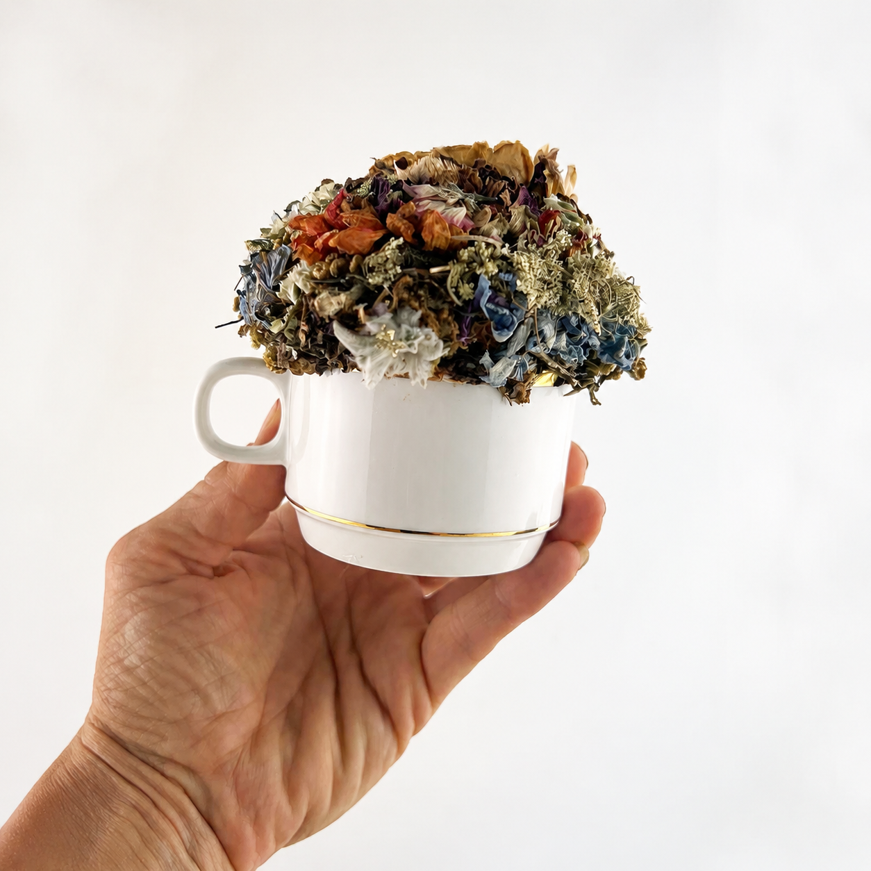 Handmade teacup arrangement featuring rust, blue, cream and brown dried botanicals held in a hand.