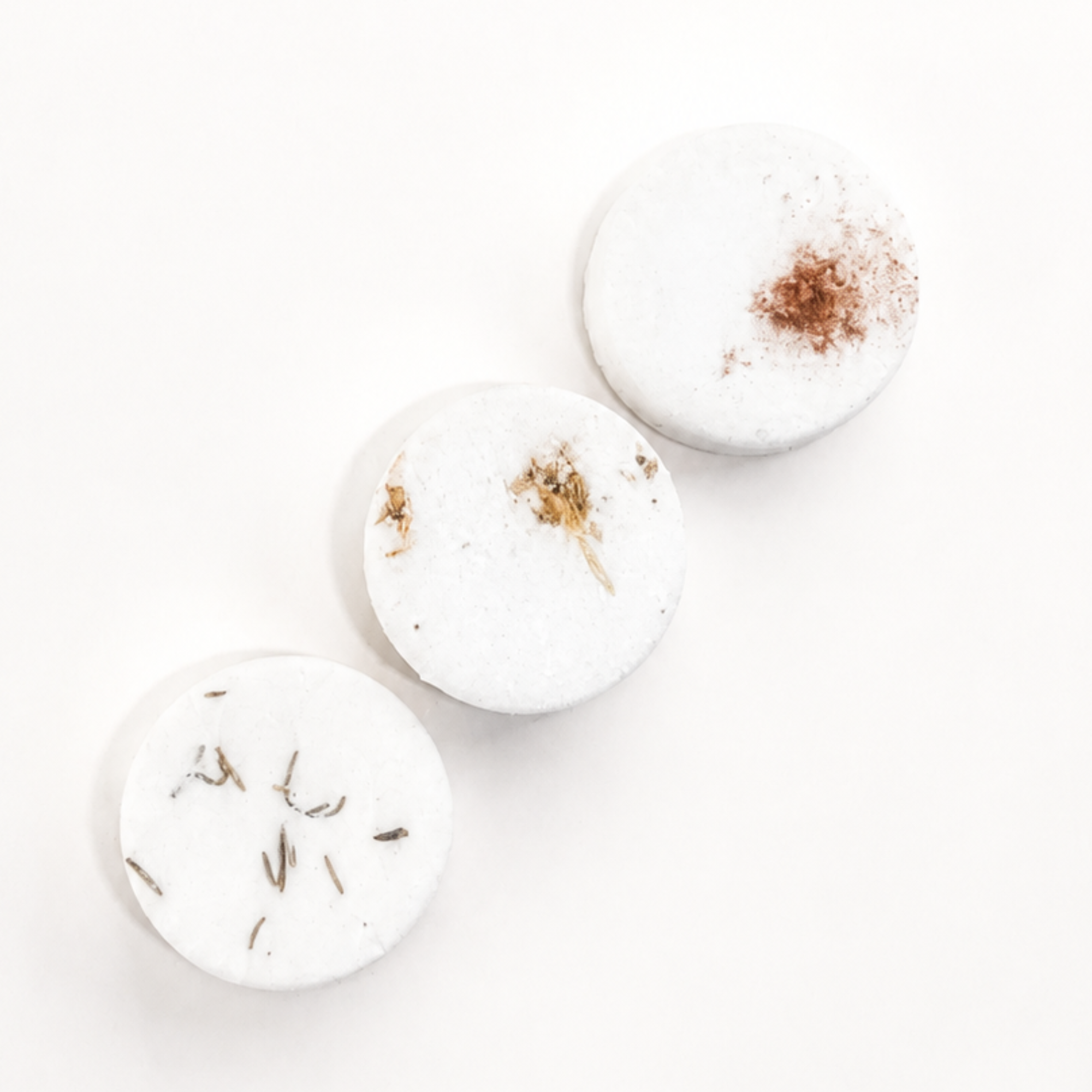 Close-up of three handcrafted Christmas shower steamers infused with rosemary, marshmallow and cinnamon botanicals on a bright white background.