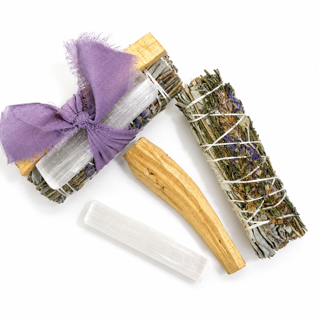 Flat lay of handcrafted White Sage Protection Ritual Bundles featuring White Sage, a lavender smudge stick, genuine Selenite cleansing wand, Palo Santo stick and a soft lavender ribbon arranged on a bright white background. Handmade spiritual cleansing gift set by Sow the Magic