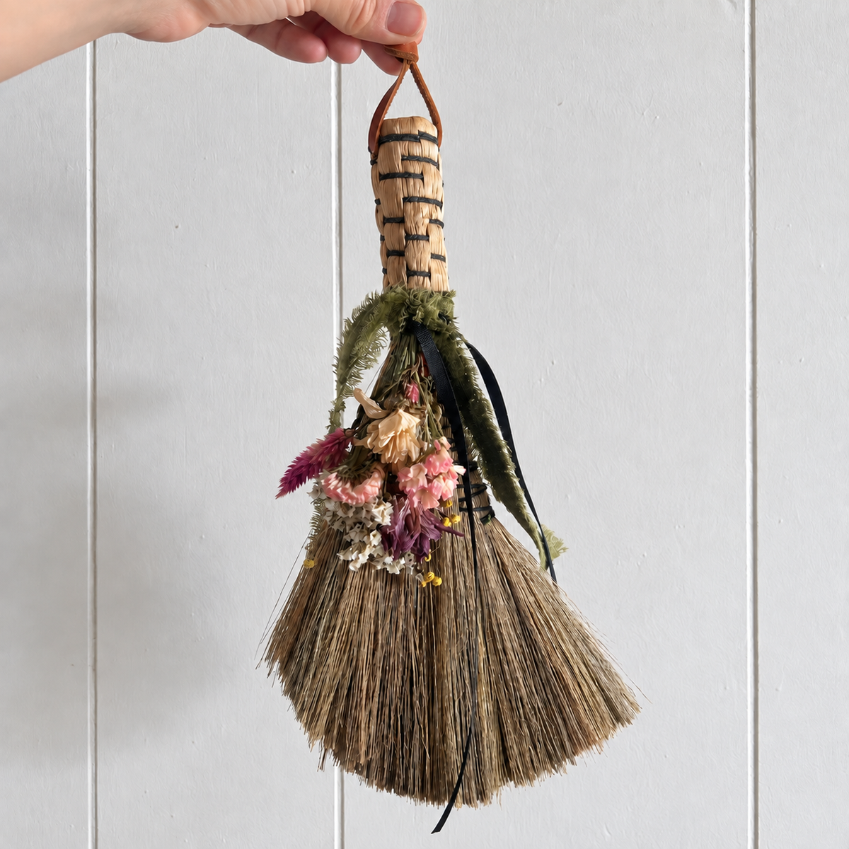 Handheld view of The Woodland Keeper’s decorative broom featuring a natural bristle base, dried farm-grown botanicals and flowing ribbons.