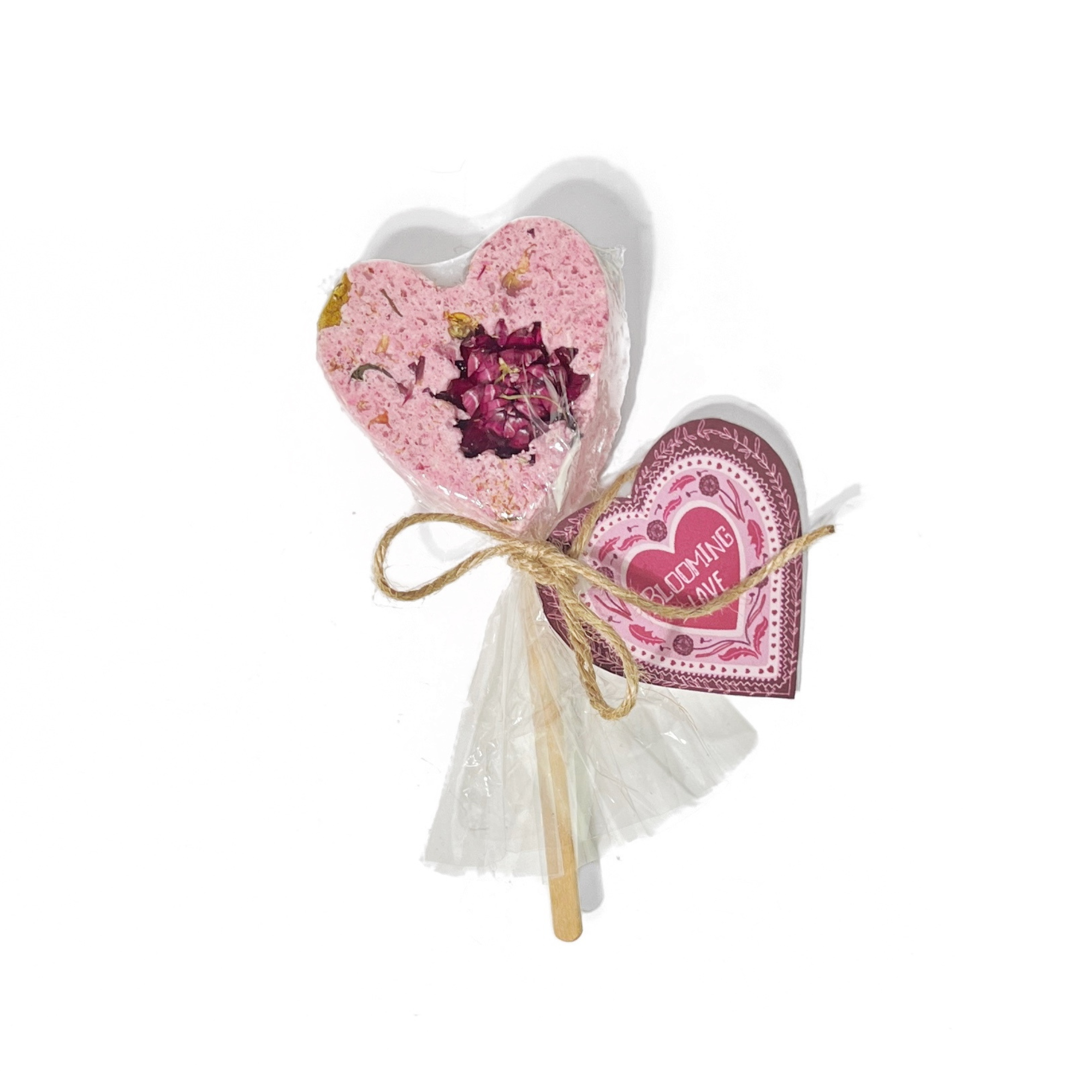 Heart-shaped pink bath clay pop with dried flower center and “Blooming Love” tag tied with twine.