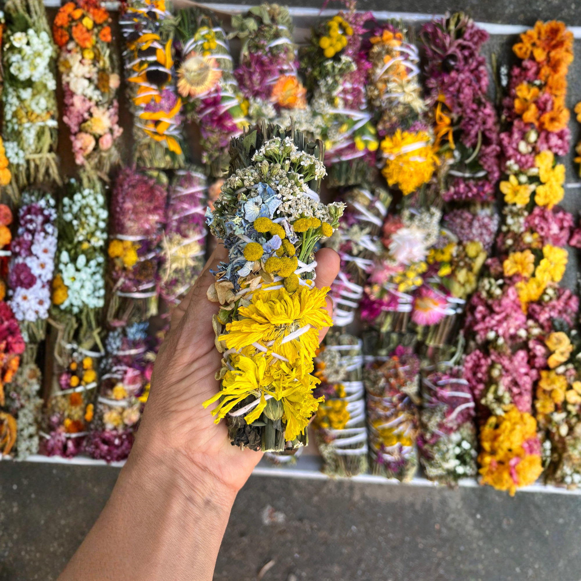 Hand selecting a colorful botanical herbal wafting wand from a display of dried flower designs