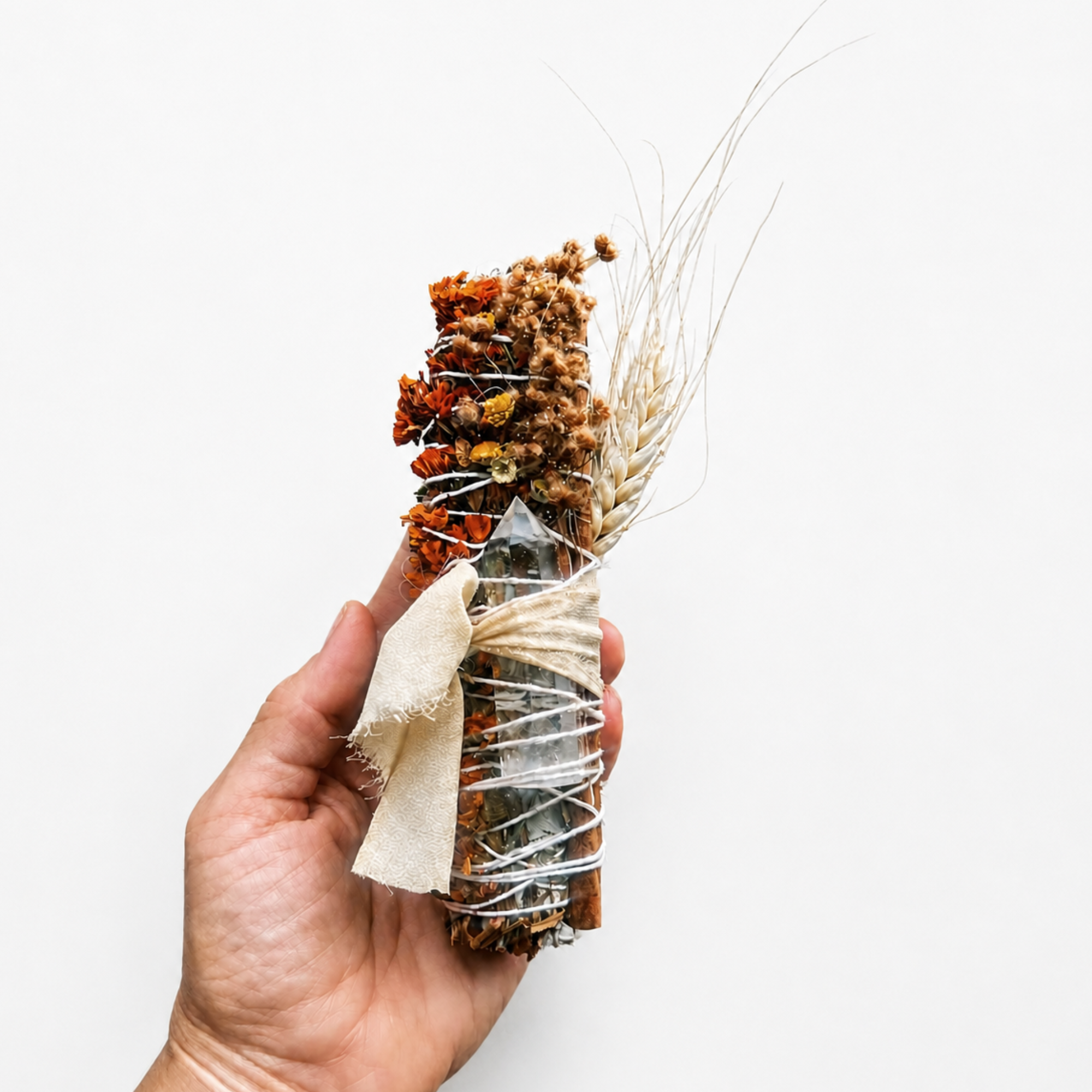 Hand holding a handcrafted botanical smoke cleansing wand wrapped with dried flowers, herbs and natural twine