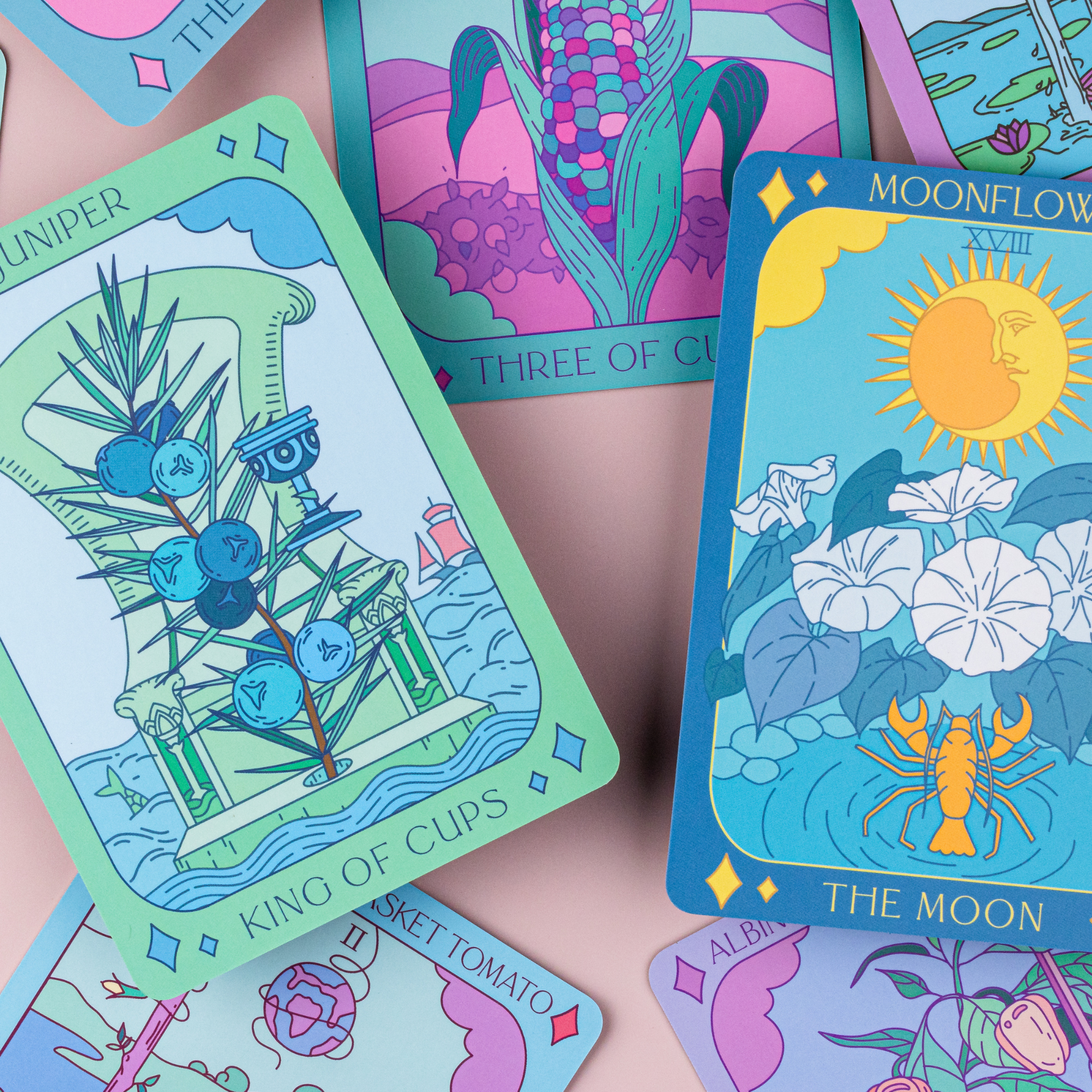 Flat lay of Botanical Tarot cards showing King of Cups, Moonflower, and Three of Cups in vibrant plant designs.