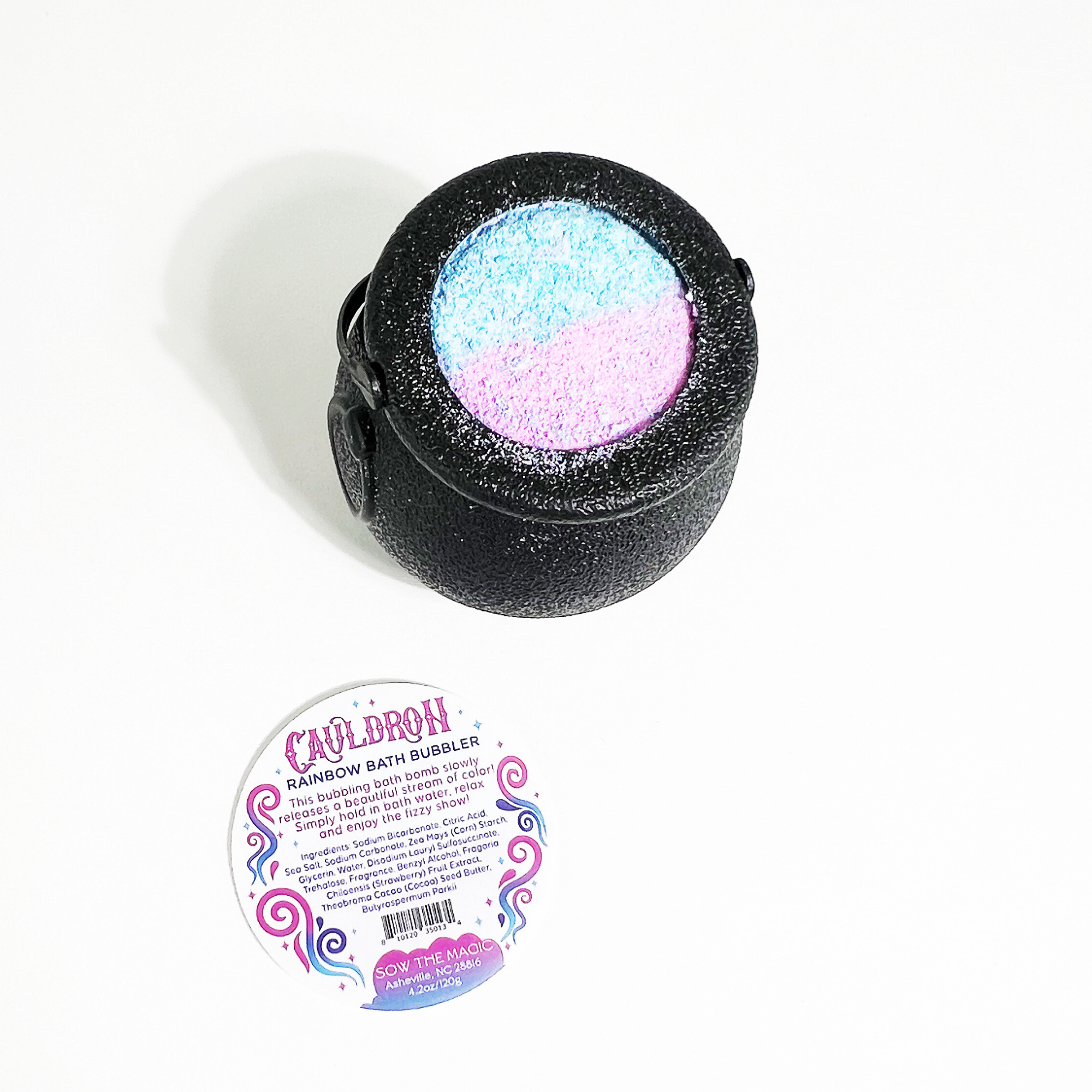 Flatlay of rainbow cauldron bath bomb with Sow the Magic label on white background