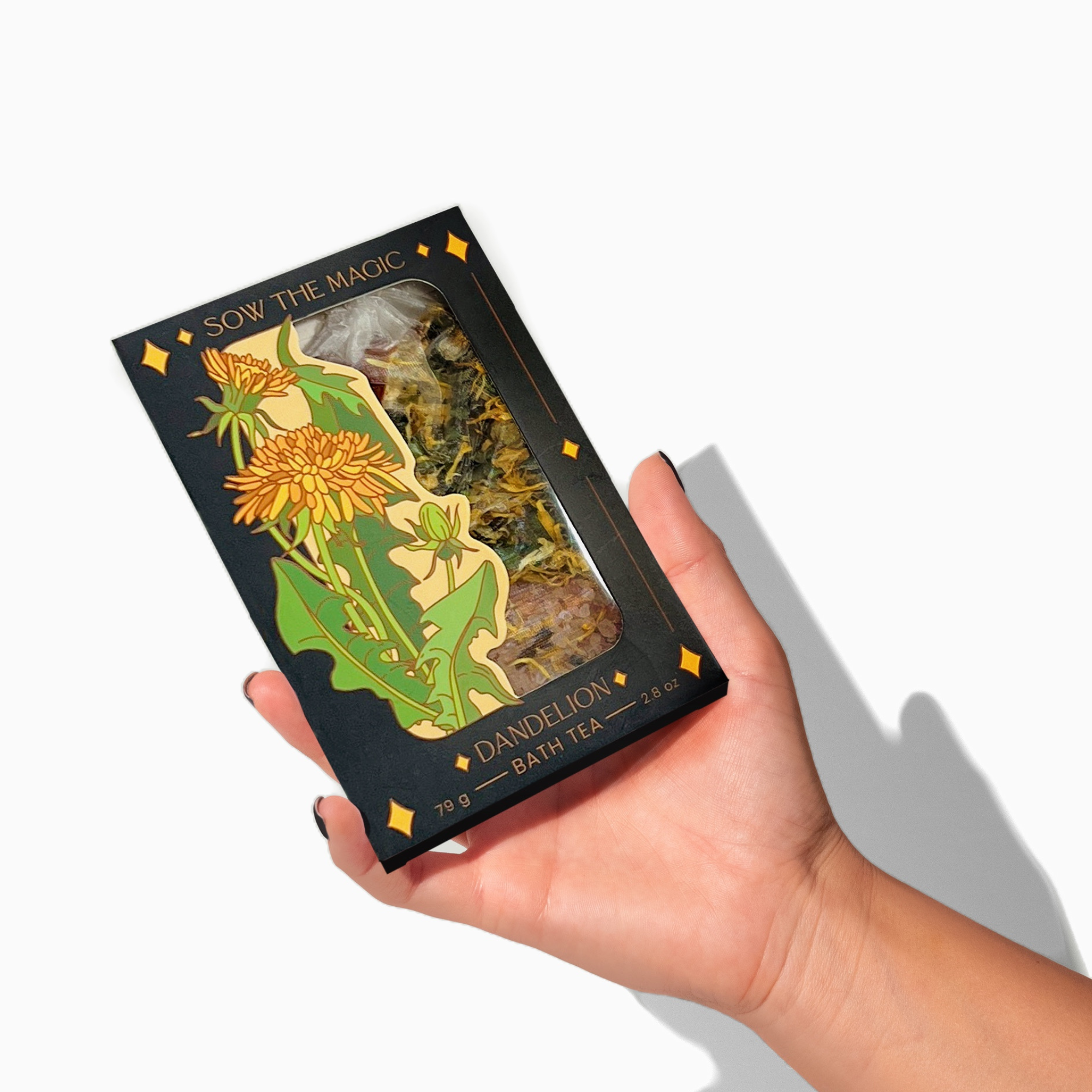 Hand holding a Dandelion Tarot Botanical Bath Tea Box by Sow the Magic, highlighting detailed floral illustration and herbal contents.
