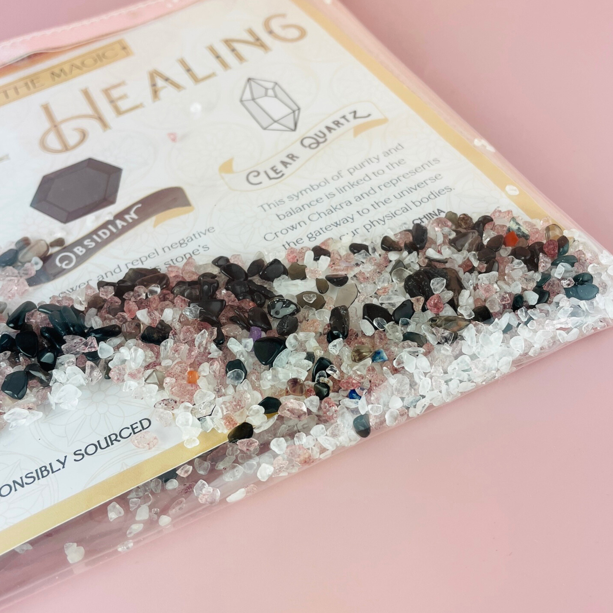 Angled view of Divine Healing Cosmetic Bag showing gemstones and gold-printed label on pink background