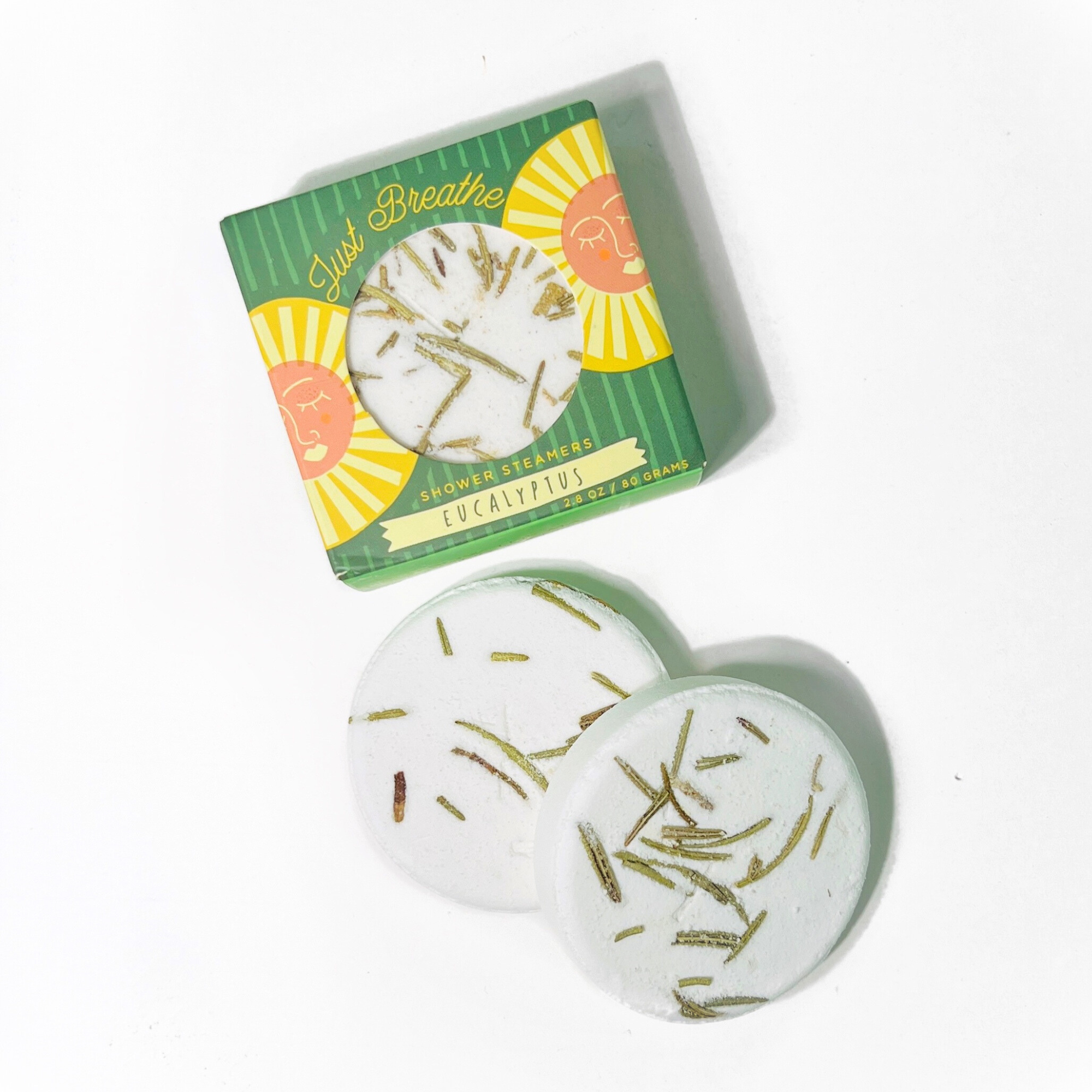 Two eucalyptus shower steamers topped with rosemary leaves beside matching green box