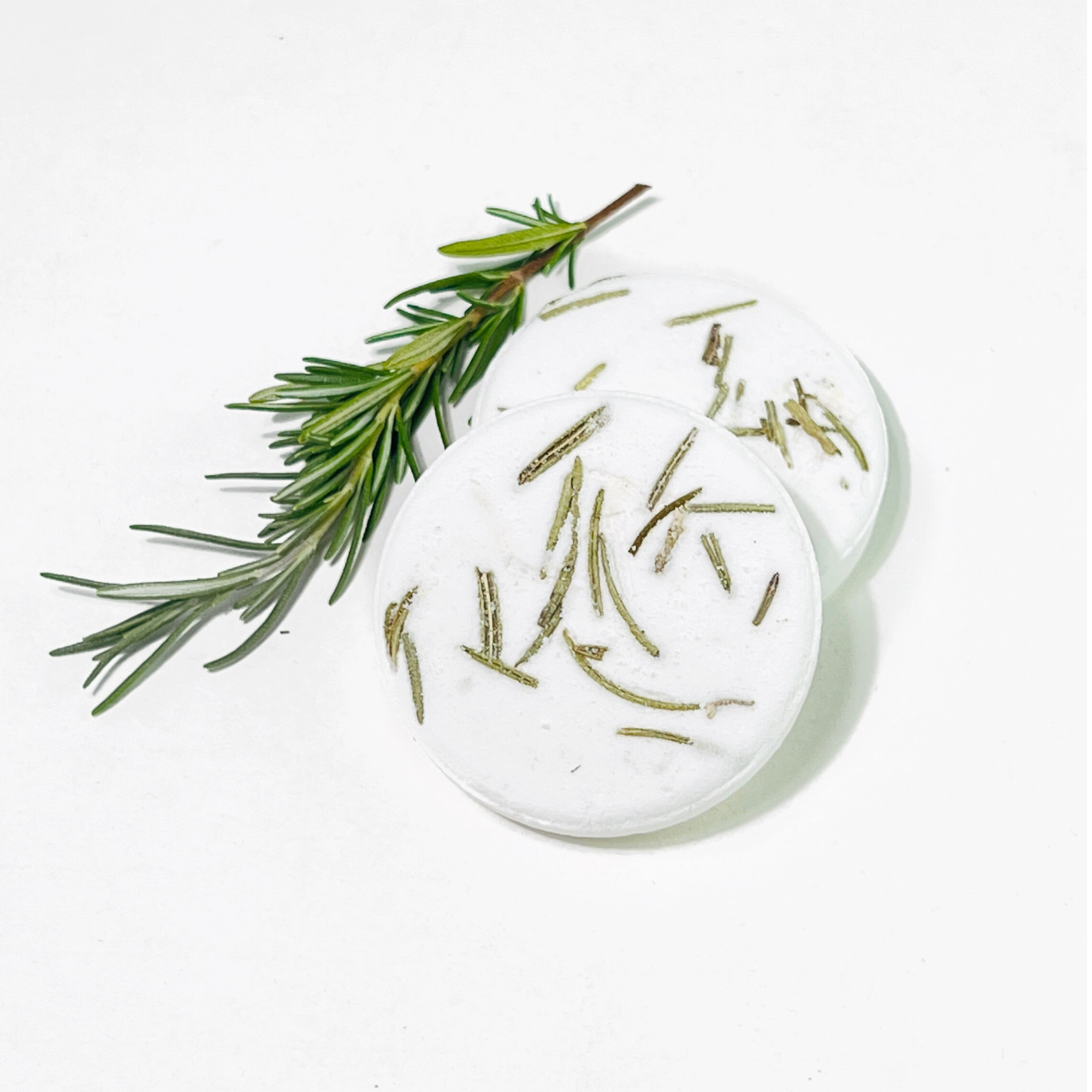 Two eucalyptus shower steamers with fresh rosemary sprig on white background