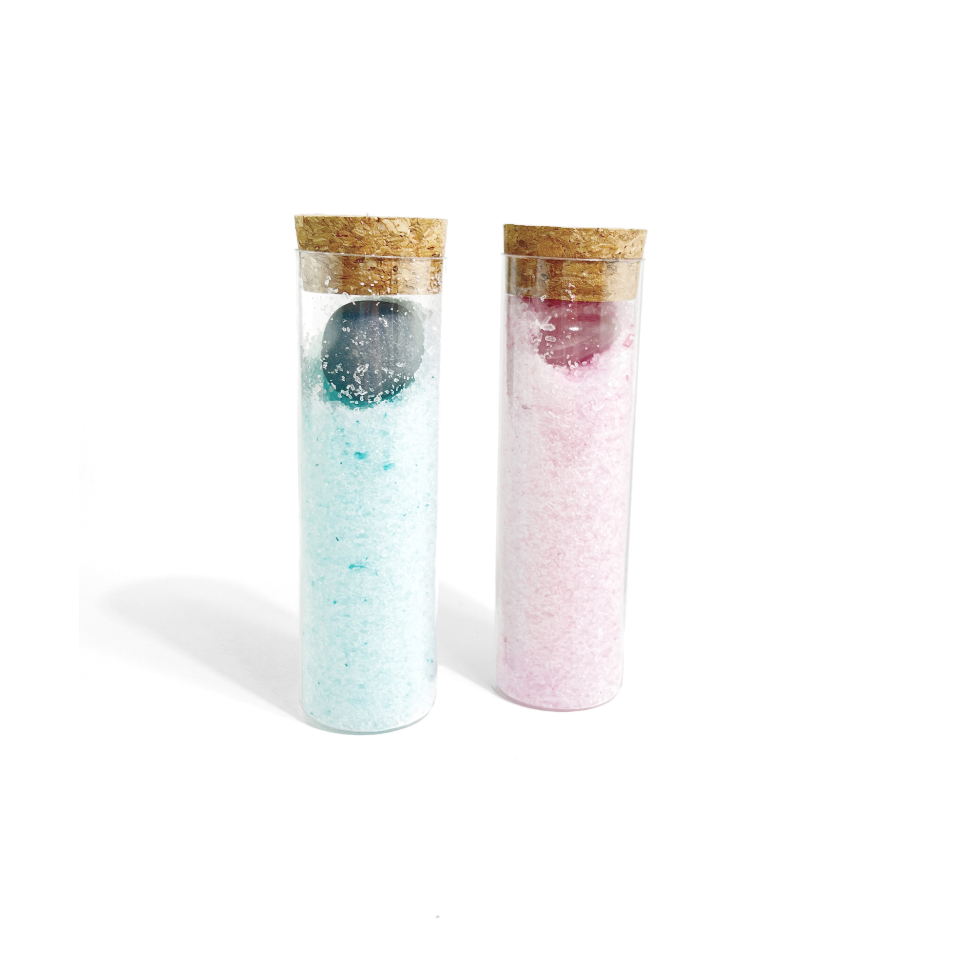 Two clear glass bath salt vials with cork lids showing blue and pink salts and visible gemstones