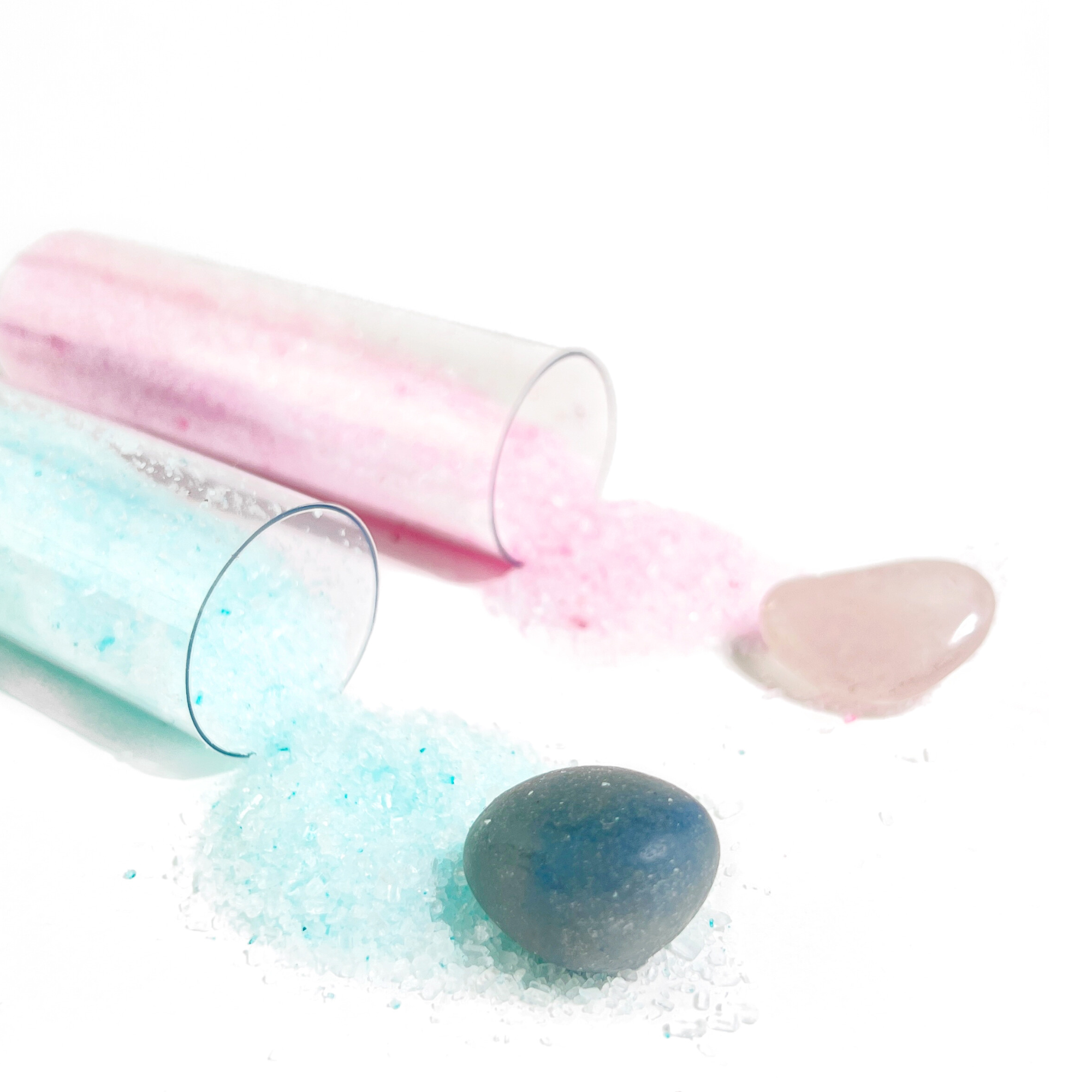 Close-up of Rose Quartz and Blue Aventurine salt soaks spilling crystals and bath salts on white surface