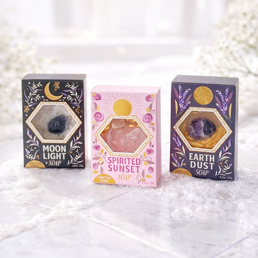 Moon Light, Spirited Sunset, and Earth Dust gemstone soaps displayed on bright marble tile with soft suds in a light airy lifestyle setting