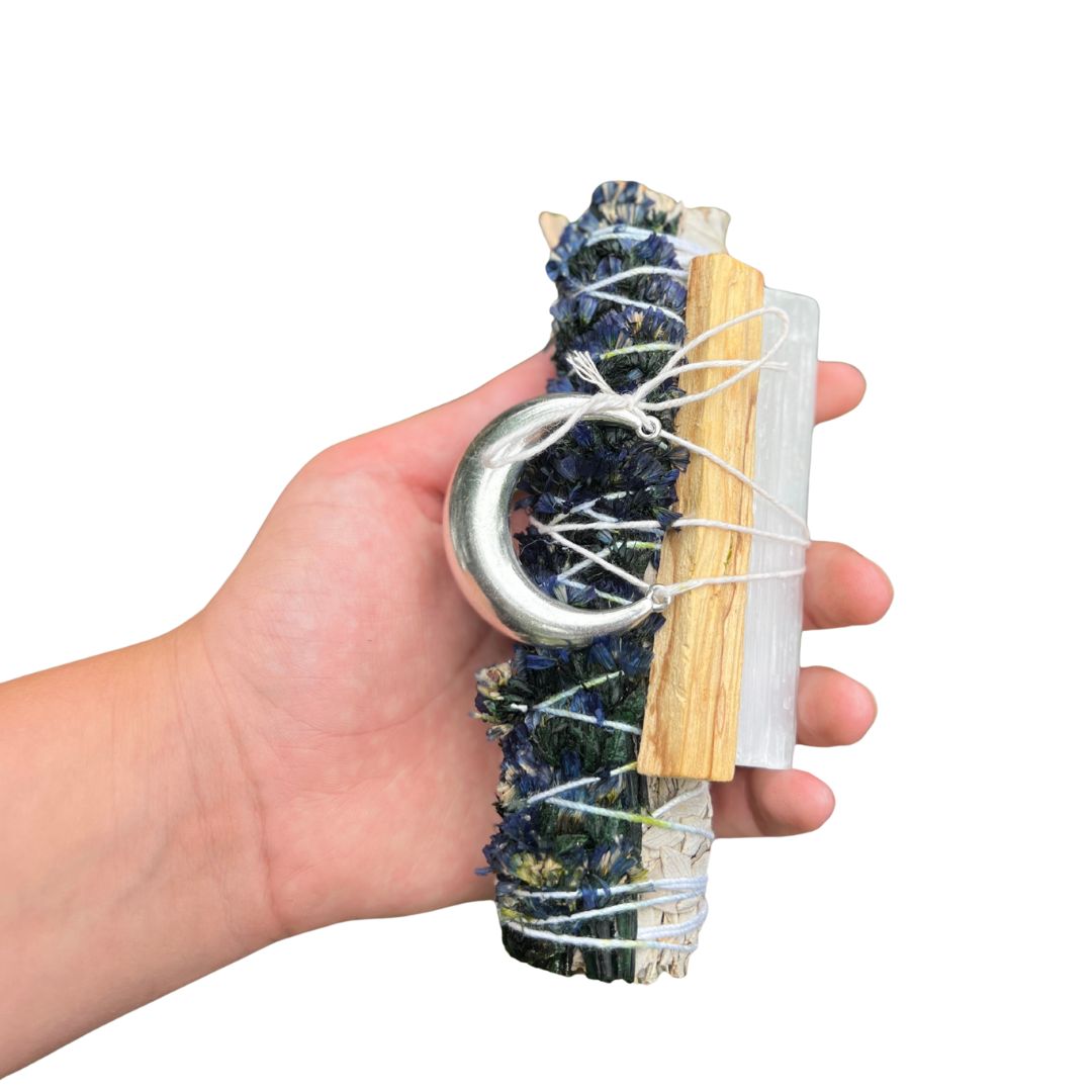 Goodnight Moon Ritual Set held in hand with white sage, blue sinuata flowers, palo santo, selenite and a silver moon charm.