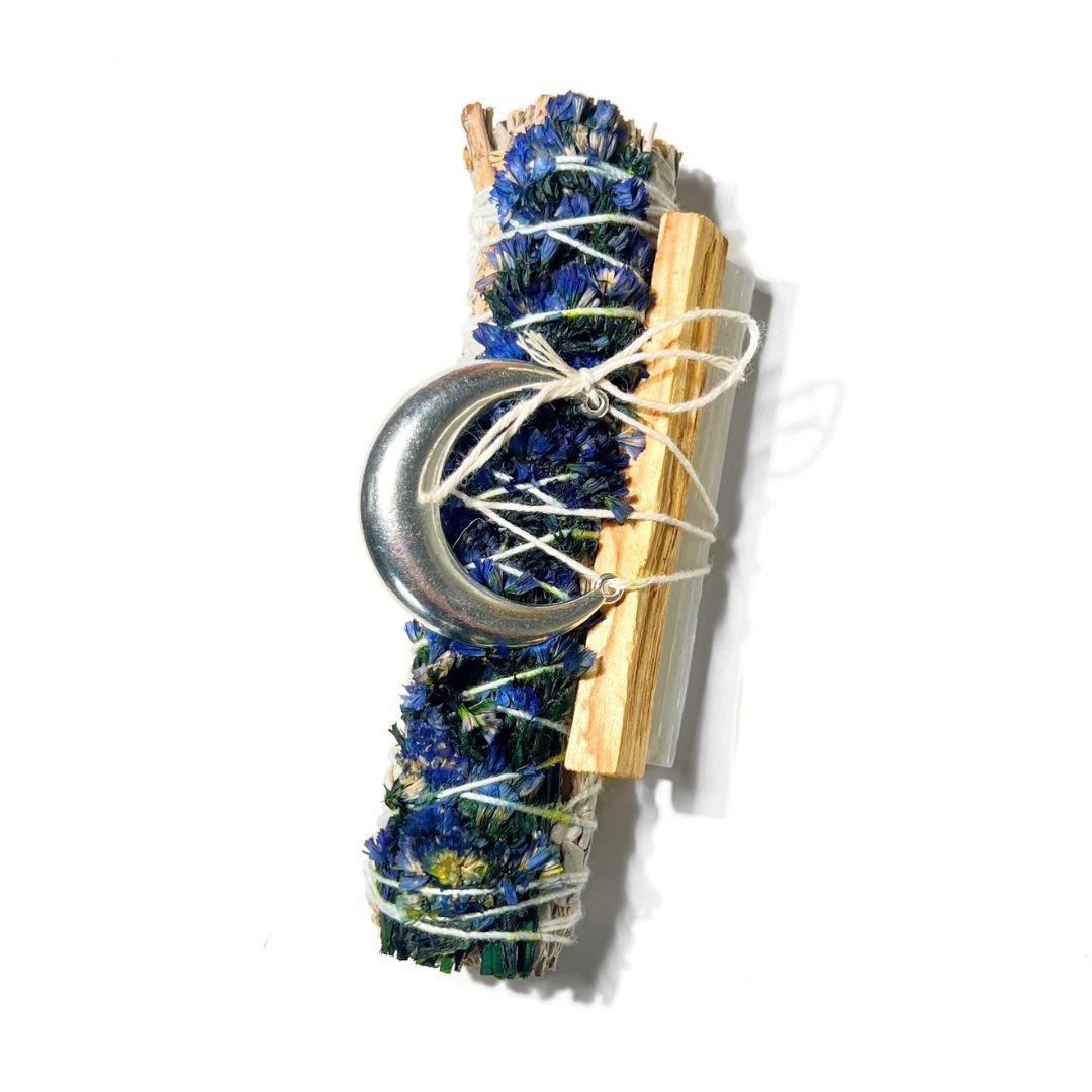 Goodnight Moon sage smudge bundle with blue flowers, palo santo, selenite and a silver moon charm on a white background.
