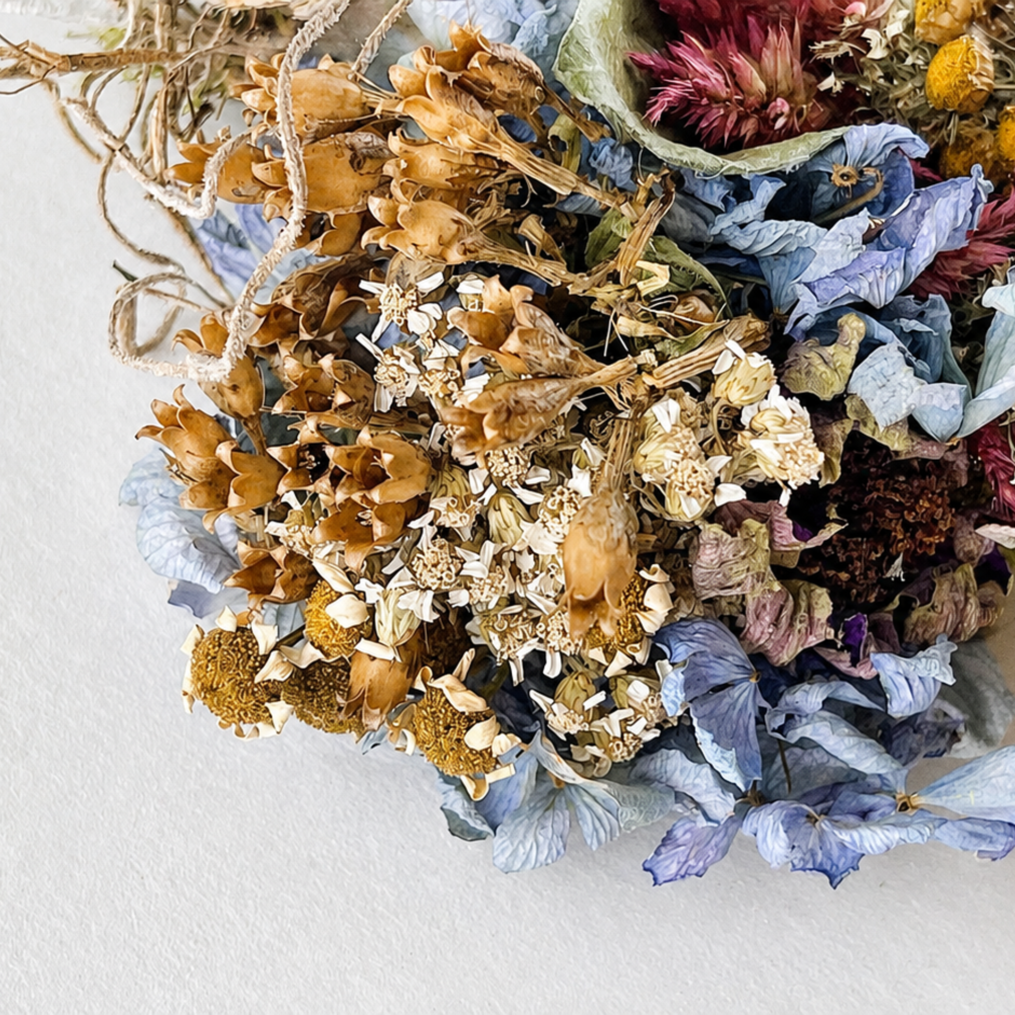 Detailed view of dried blue, gold and burgundy flowers arranged in a botanical wall hanging