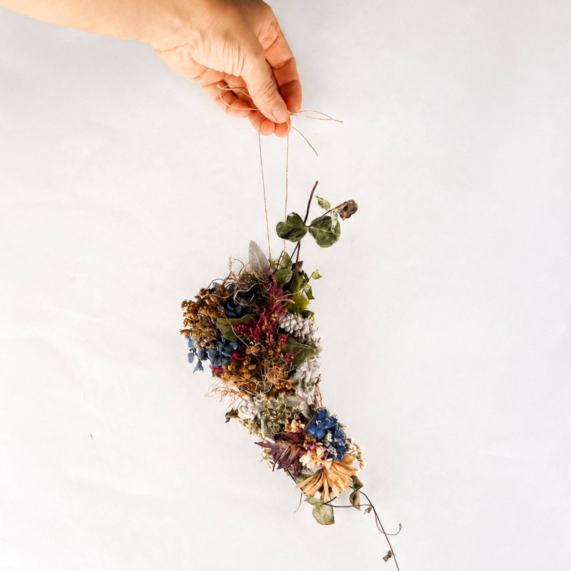 Hand holding a colorful handmade botanical wall hanging by its natural twine loop