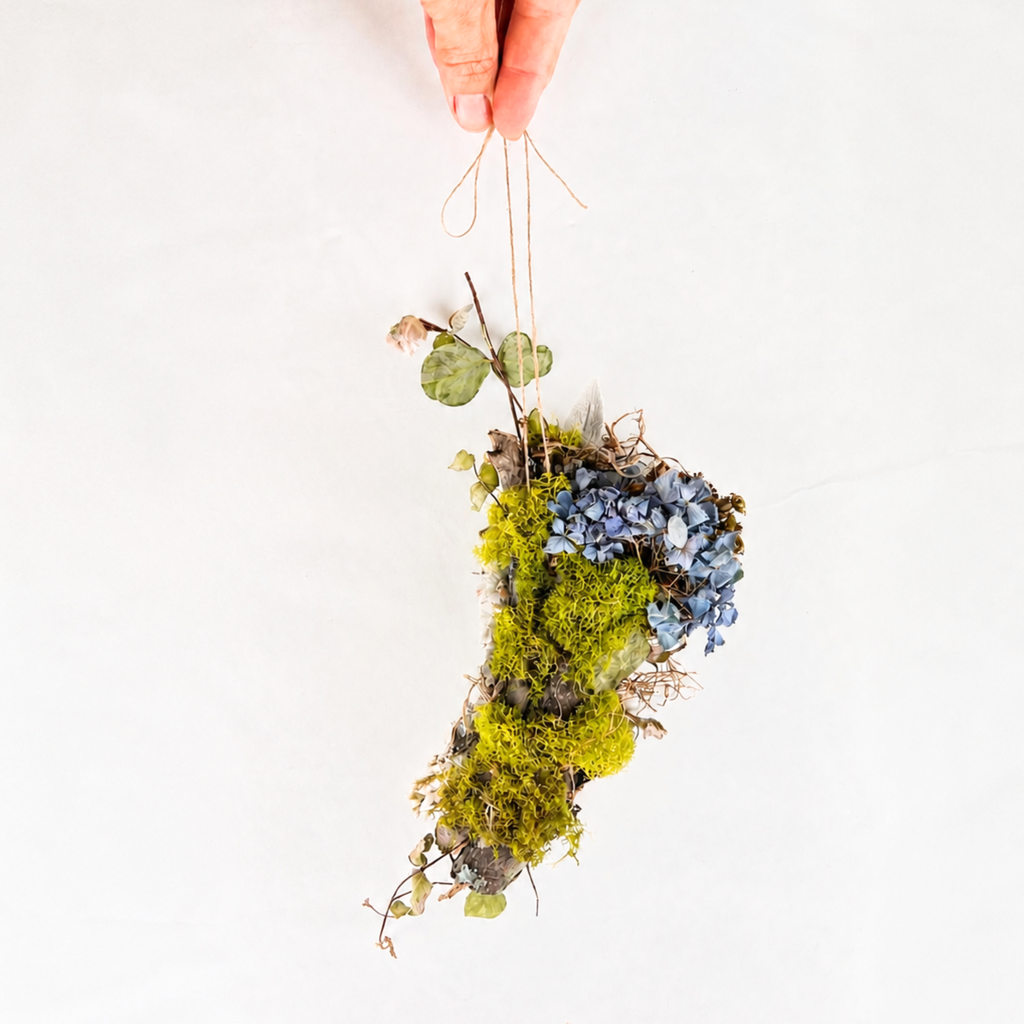Back view of a handmade botanical wall hanging featuring preserved moss, blue flowers and dried leaves