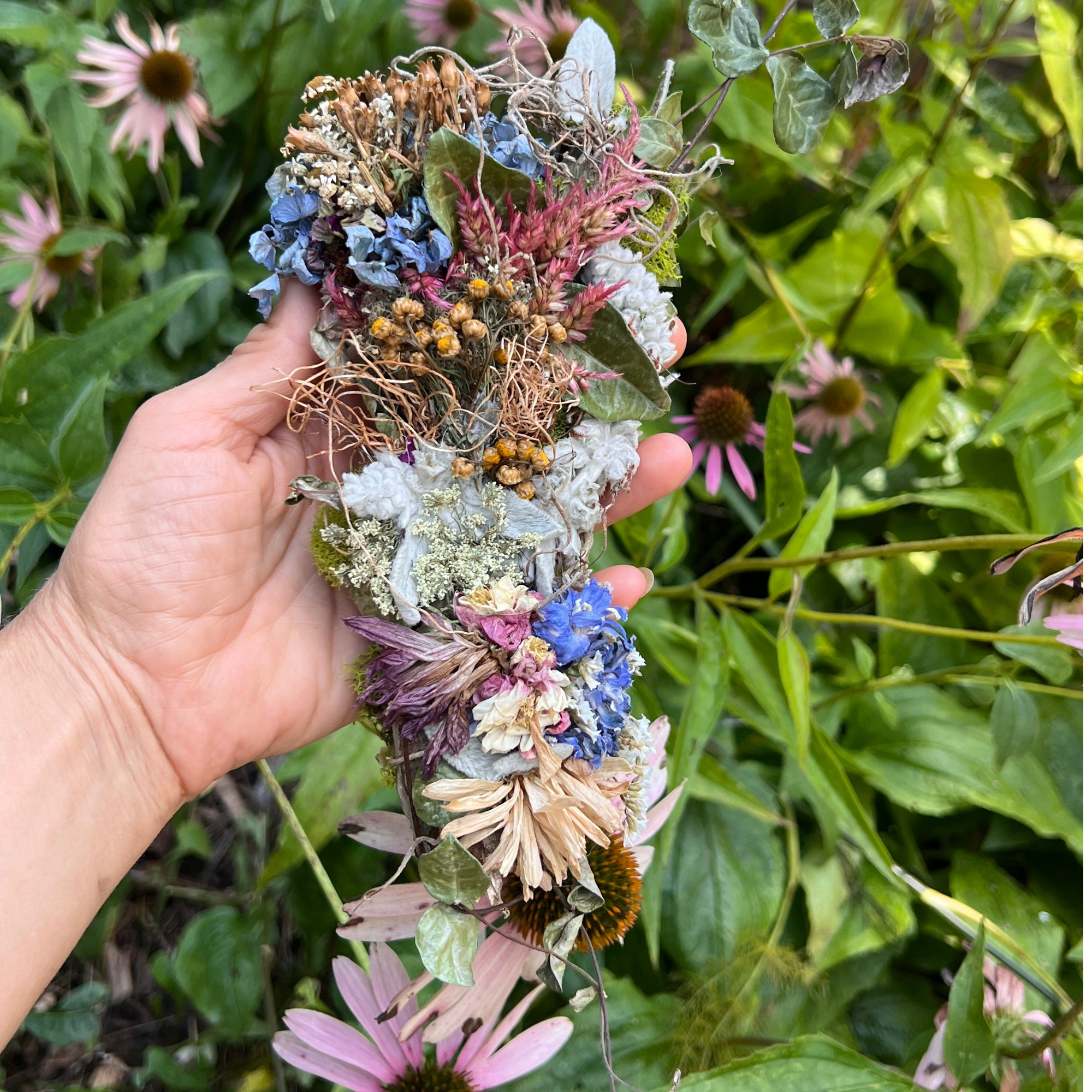 Handmade dried flower wall hanging held outdoors against a lush garden background