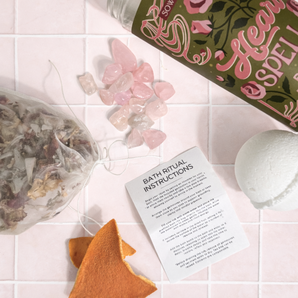 Heart Spell Bath Ritual Kit components styled on pale pink tile with rose quartz, bath tea, bath bomb, dried citrus and instructions