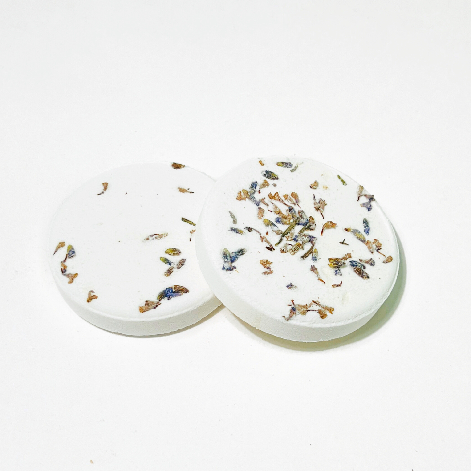 Closeup of two lavender shower steamers topped with dried lavender petals on white background