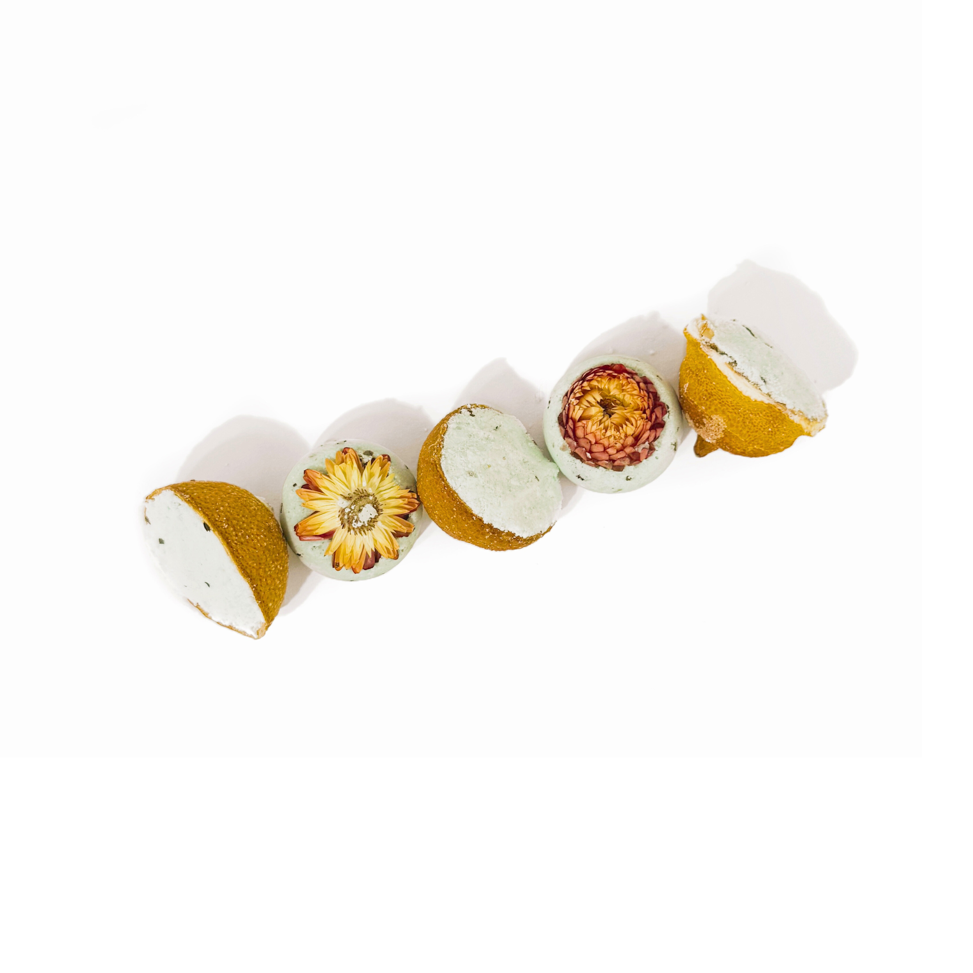 Flat lay lineup of Lemon Drop bath bombs with dried lemons and bright yellow flowers on a white background