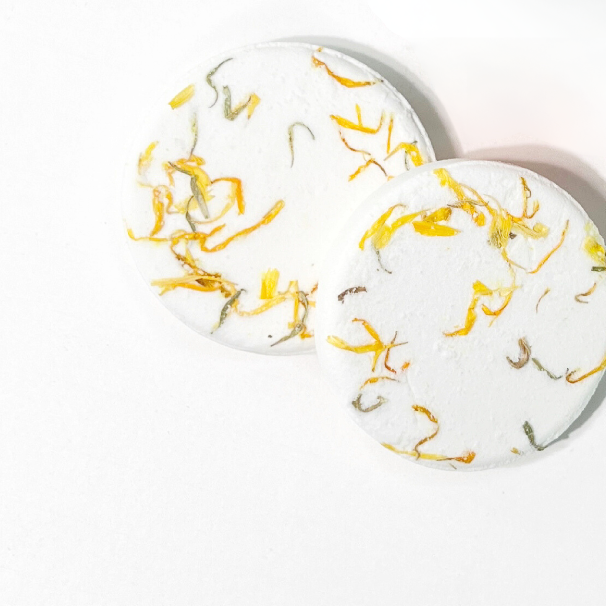 Two lemongrass shower steamers topped with calendula petals on white background