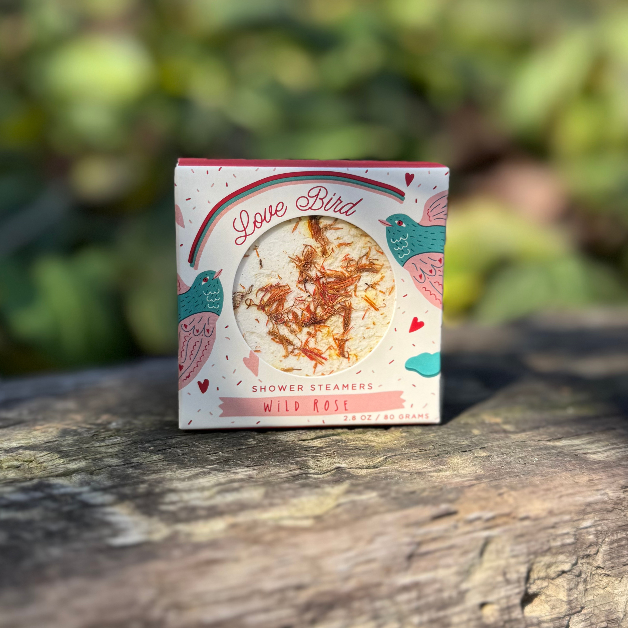 Love Bird wild rose shower steamer box displayed outdoors on rustic wood surface