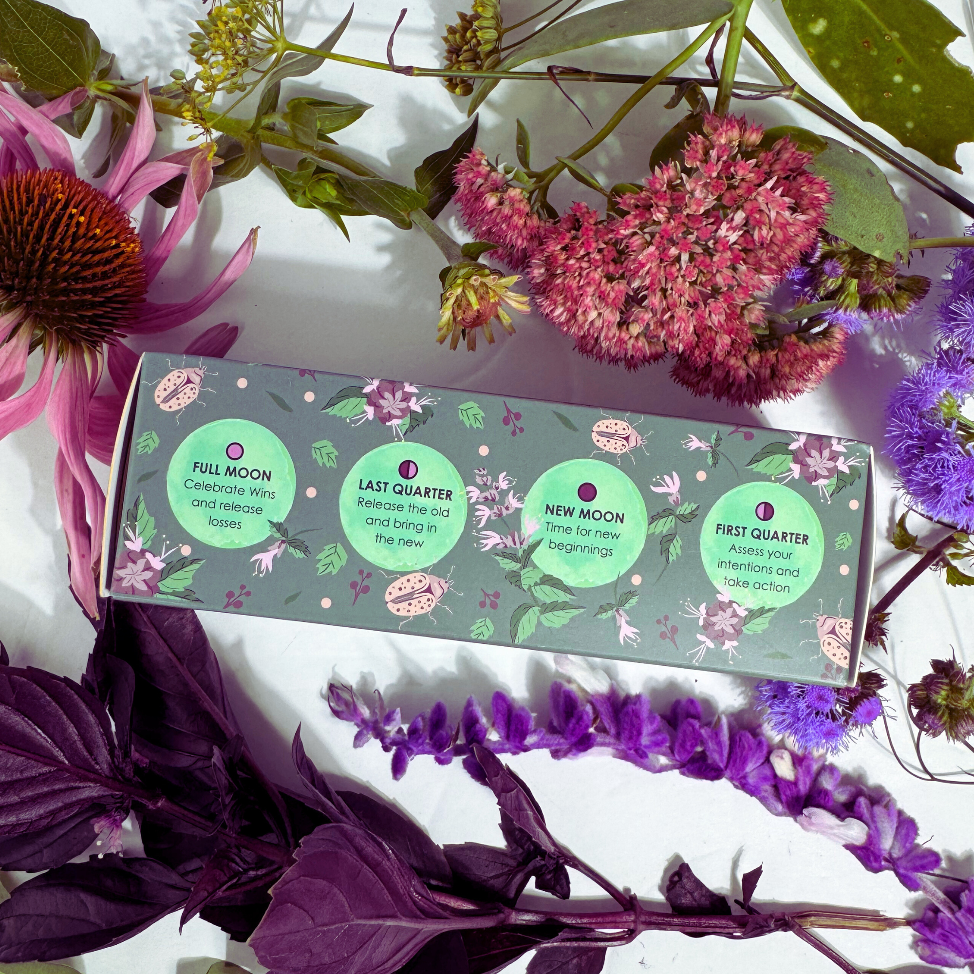 Moon Phase Protect + Purify Bath Bomb Trio box surrounded by colorful flowers showing moon phase meanings