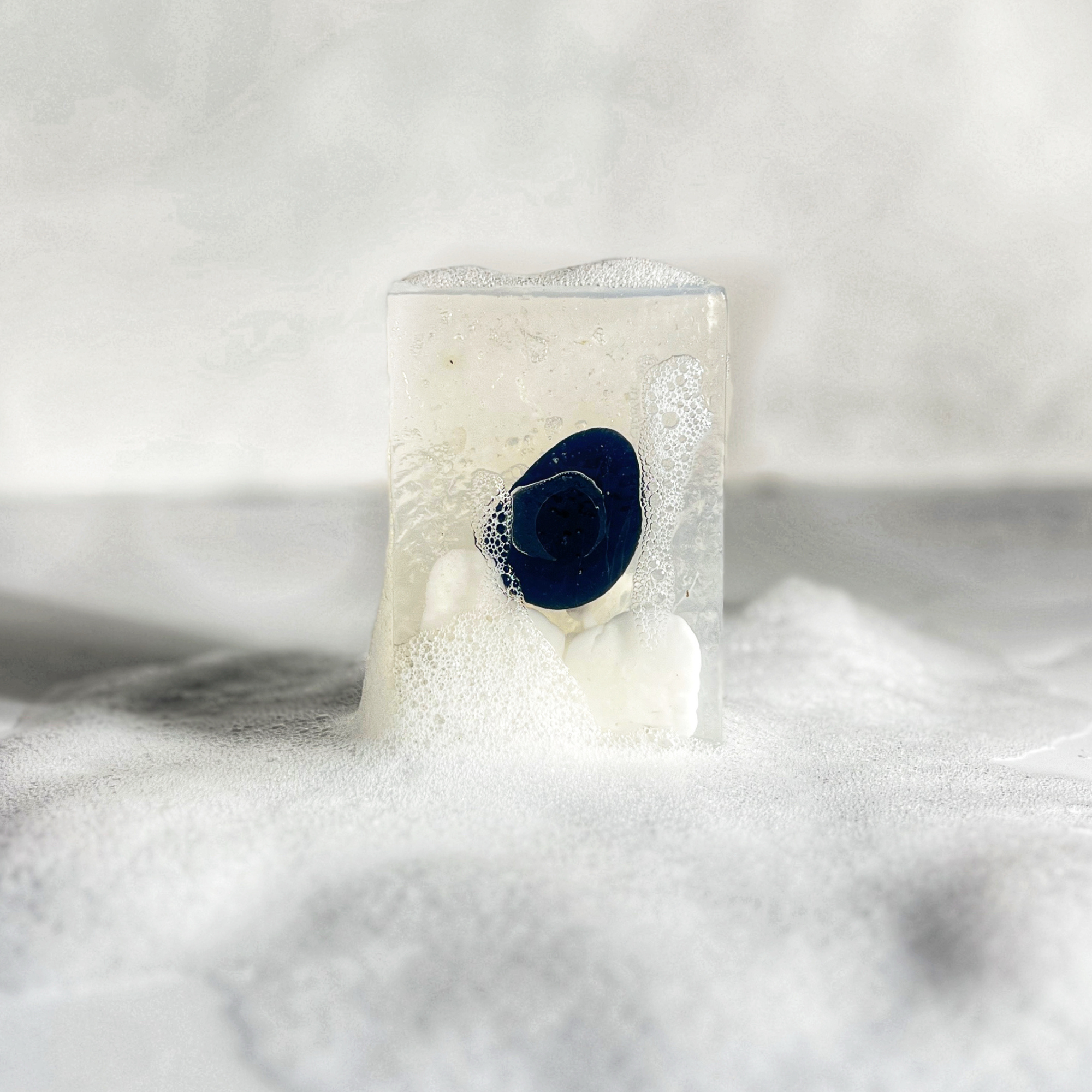 Close-up of Moonlight Gemstone Soap with visible obsidian stone surrounded by white lather and bubbles.