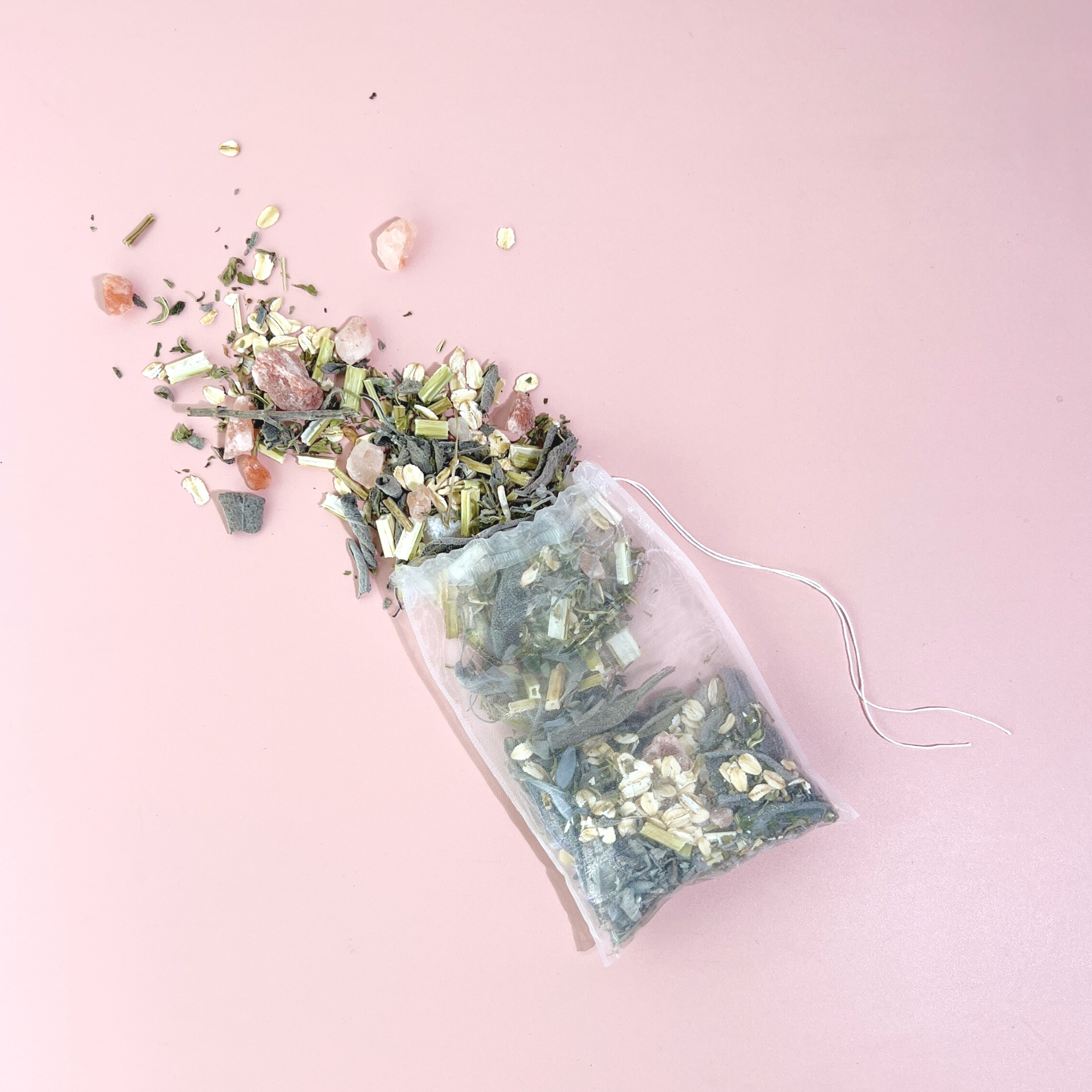 Open Motherwort Bath Tea tea bag spilling herbs, oats and pink Himalayan salt on pastel surface.