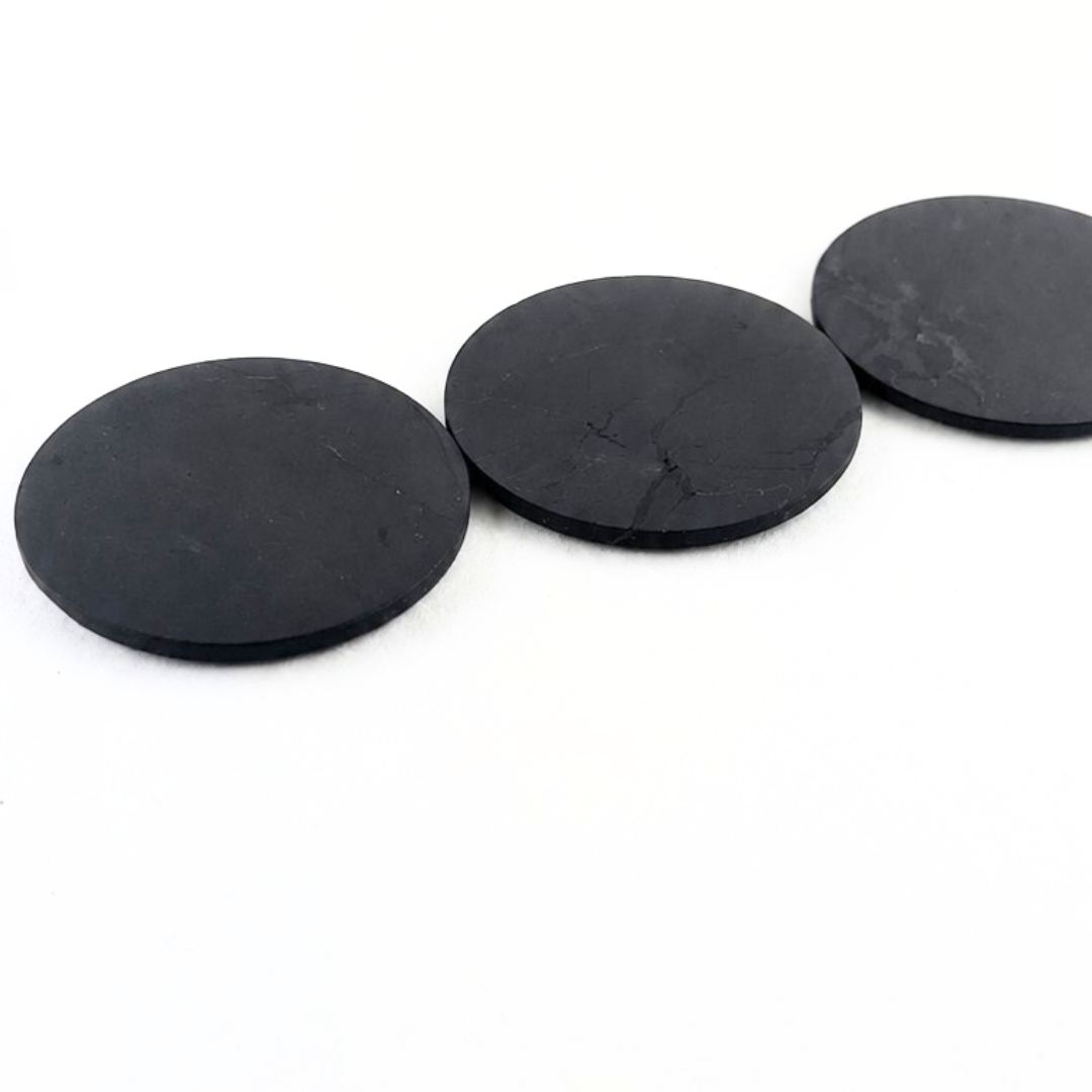 Three smooth round black Shungite stone stickers arranged in a row on a white background